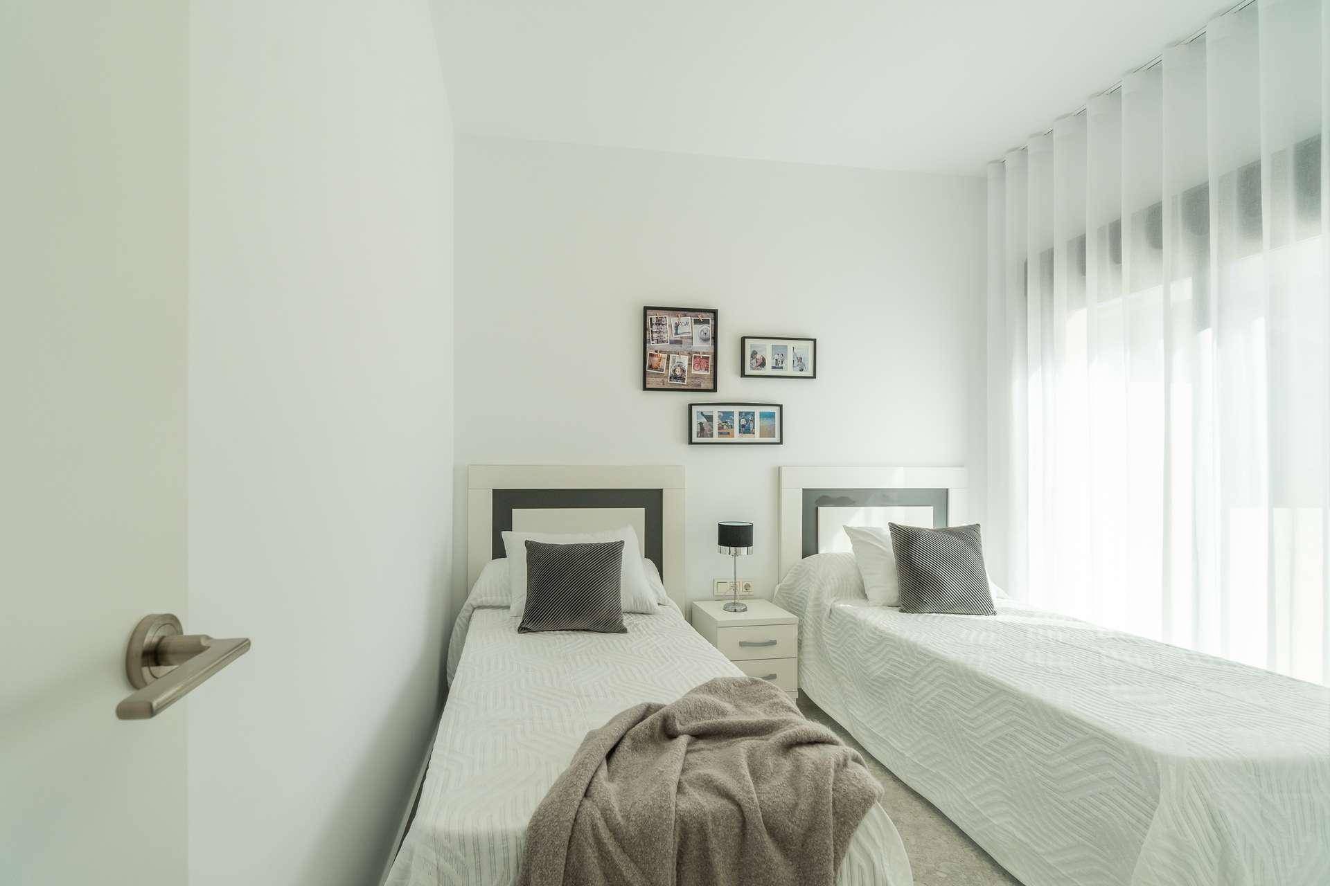 Helles Schlafzimmer mit zwei Einzelbetten, weißen Wänden und Vorhängen für viel Tageslicht.