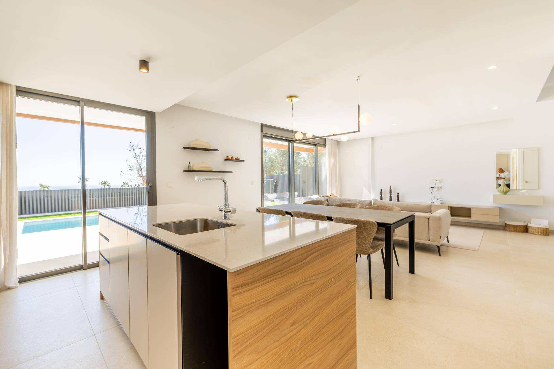 Heller offener Wohnbereich mit moderner Küche, Kochinsel und direktem Zugang zur Poolterrasse.