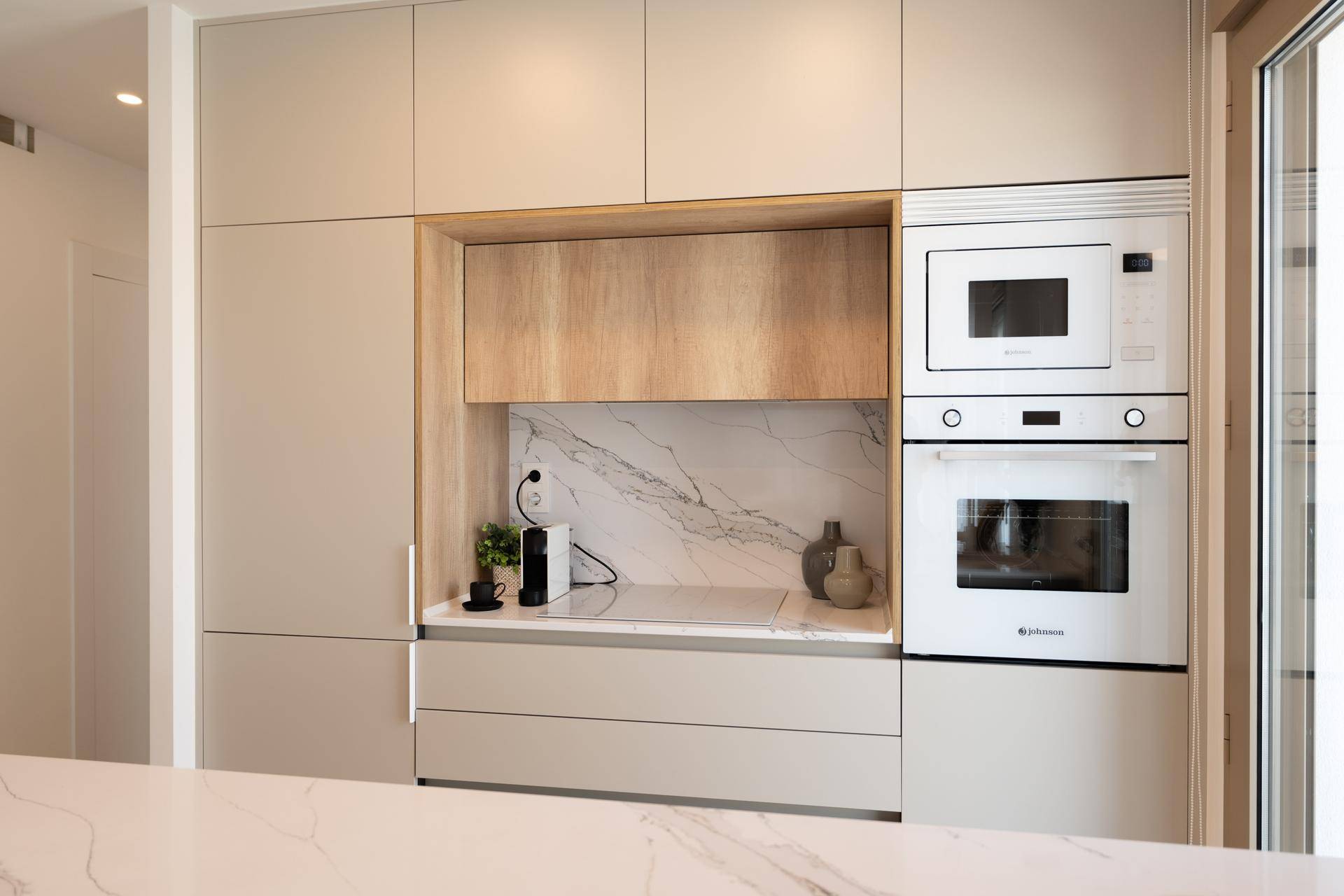 Detailansicht der modernen Küche mit integriertem Backofen, Mikrowelle und Marmor-Rückwand.
