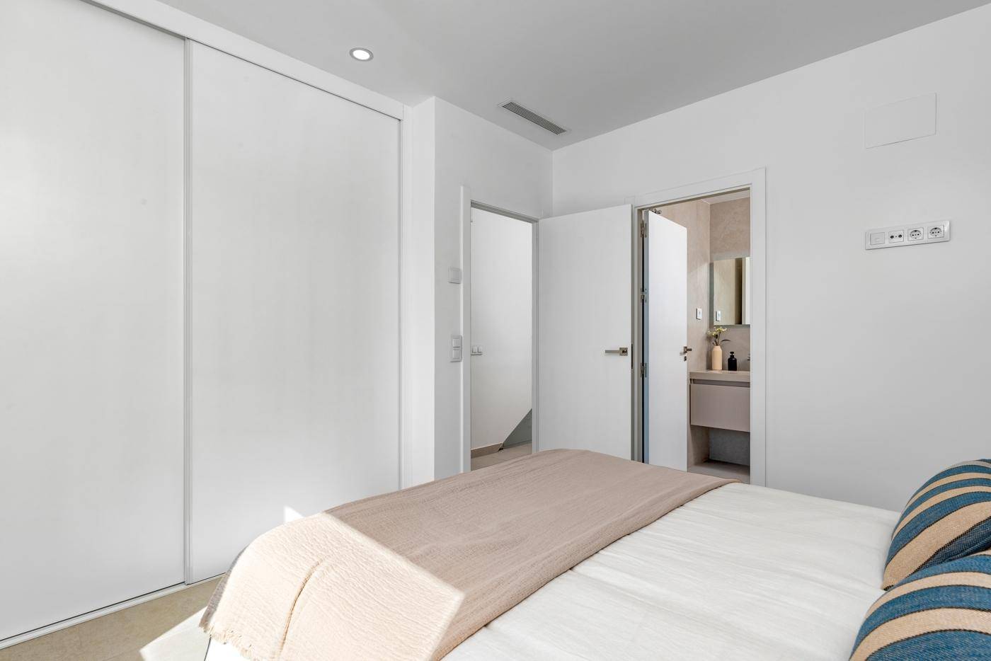 Schlafzimmer mit weißem Einbauschrank und offenem Zugang zu einem angrenzenden Badezimmer.