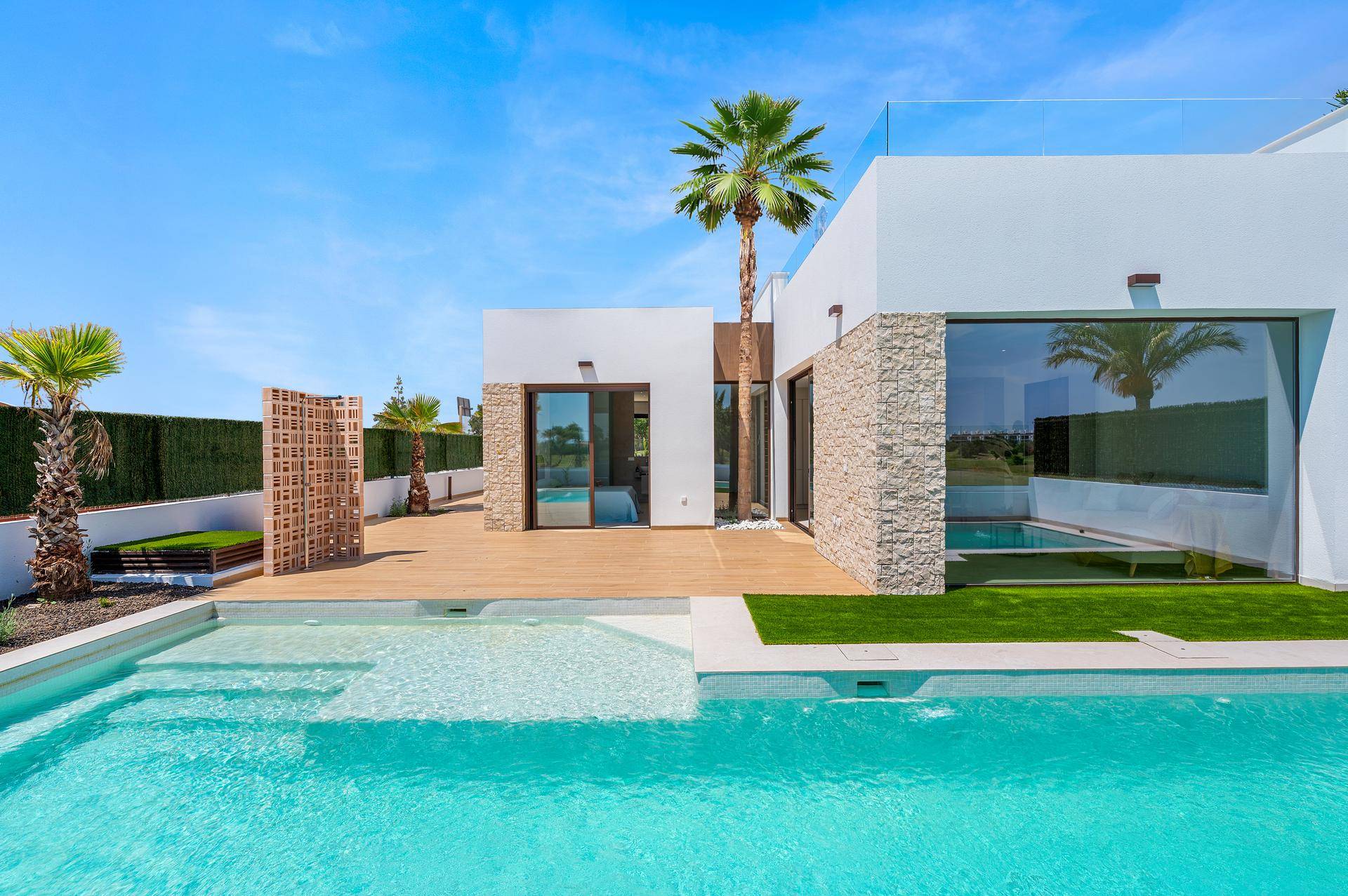 Moderne Villa mit großem Pool, Holzterrasse und raumhohen Fenstern, umgeben von Grünflächen.
