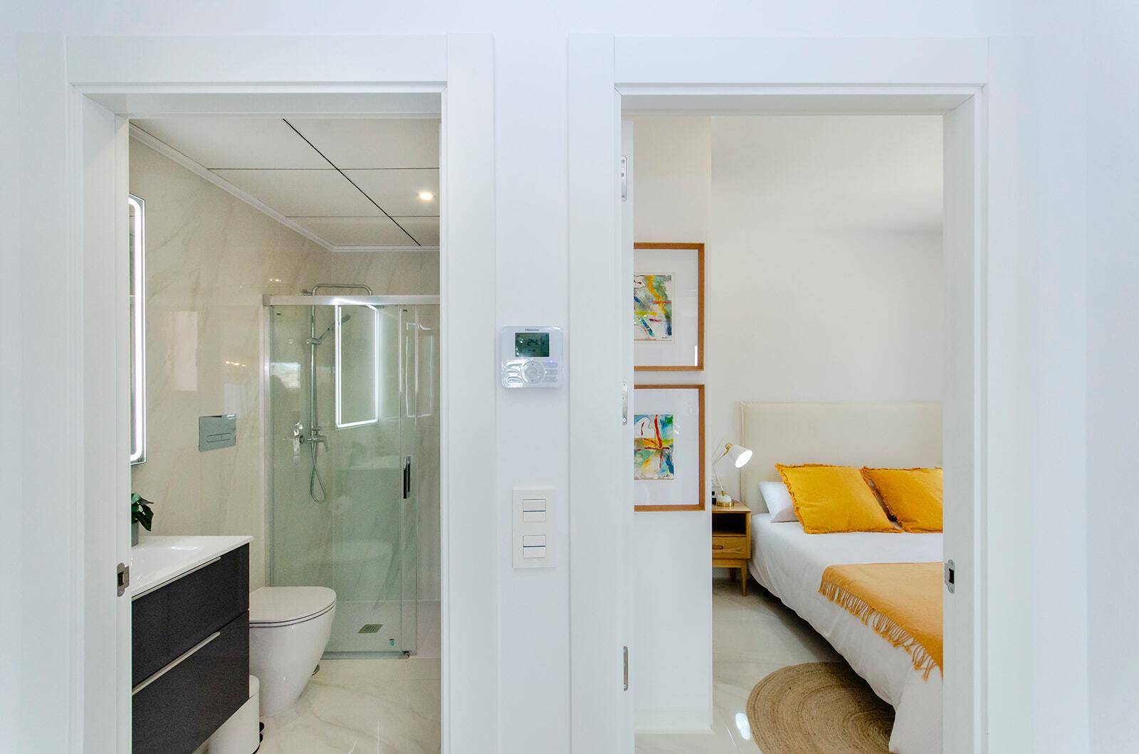 Blick durch die Tür in ein modernes Badezimmer und ein helles Schlafzimmer.