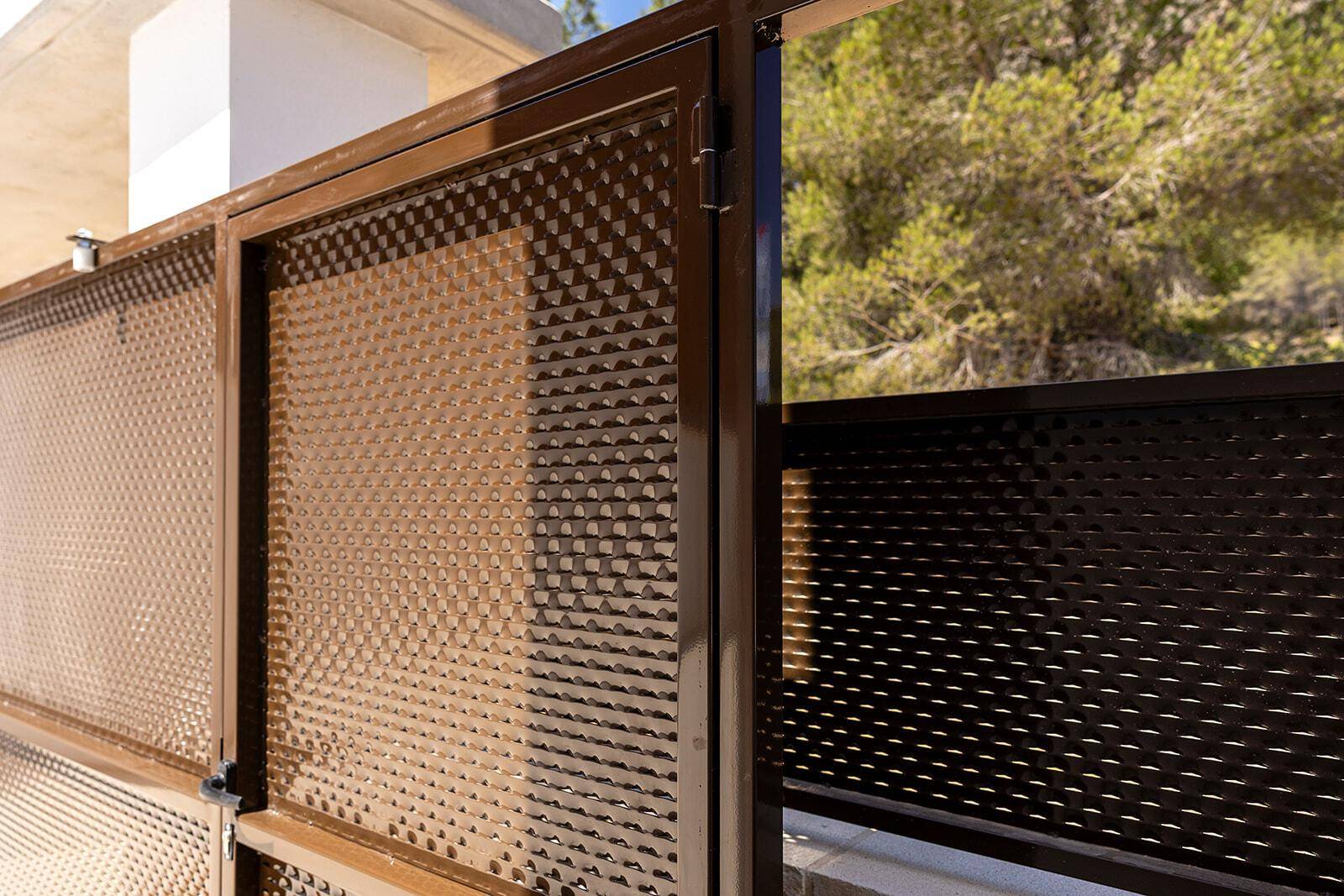 Detailansicht eines modernen Metallzauns mit perforiertem Muster in braunem Farbton.
