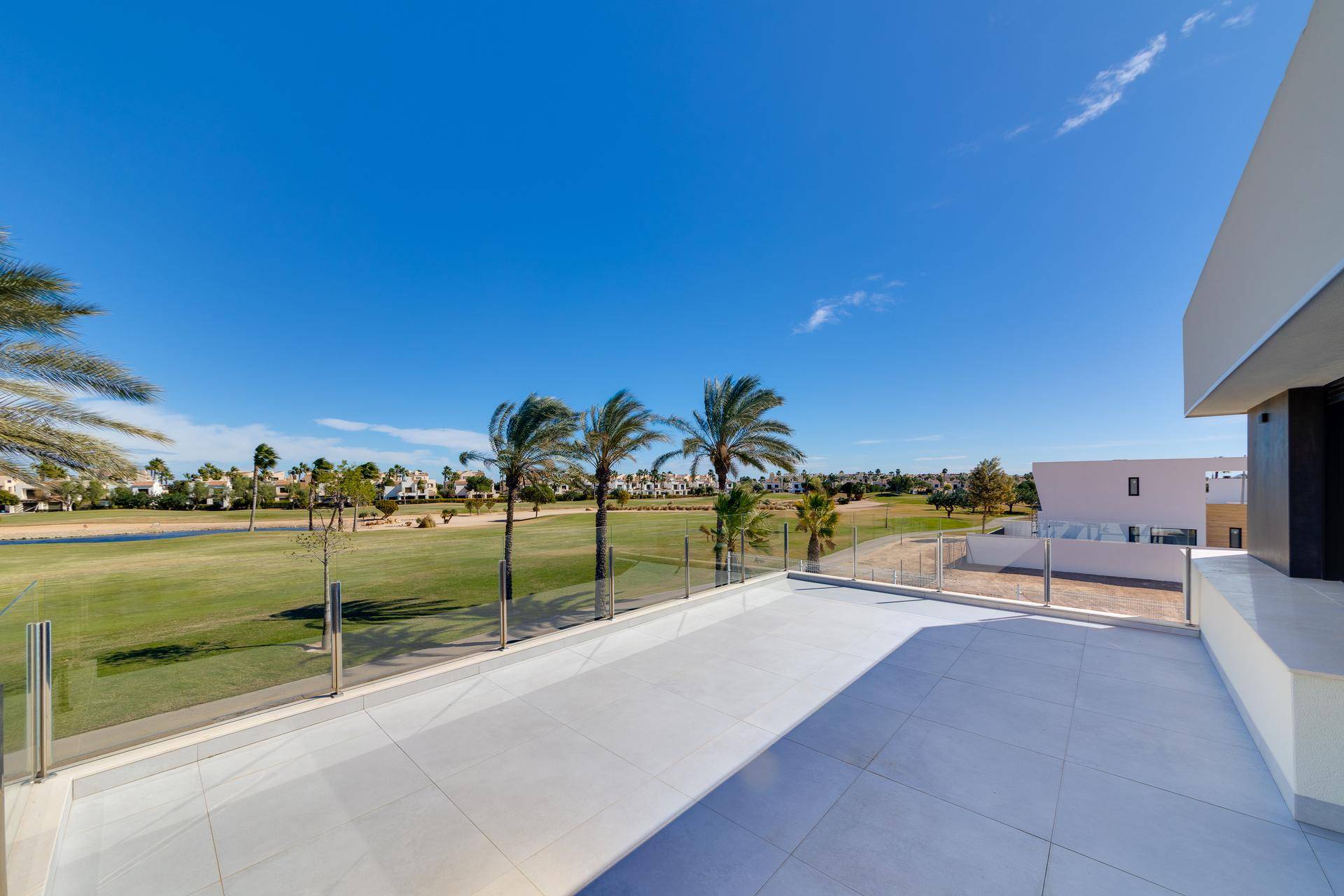 Weitläufiger Blick über einen grünen Golfplatz mit Palmen unter blauem Himmel.