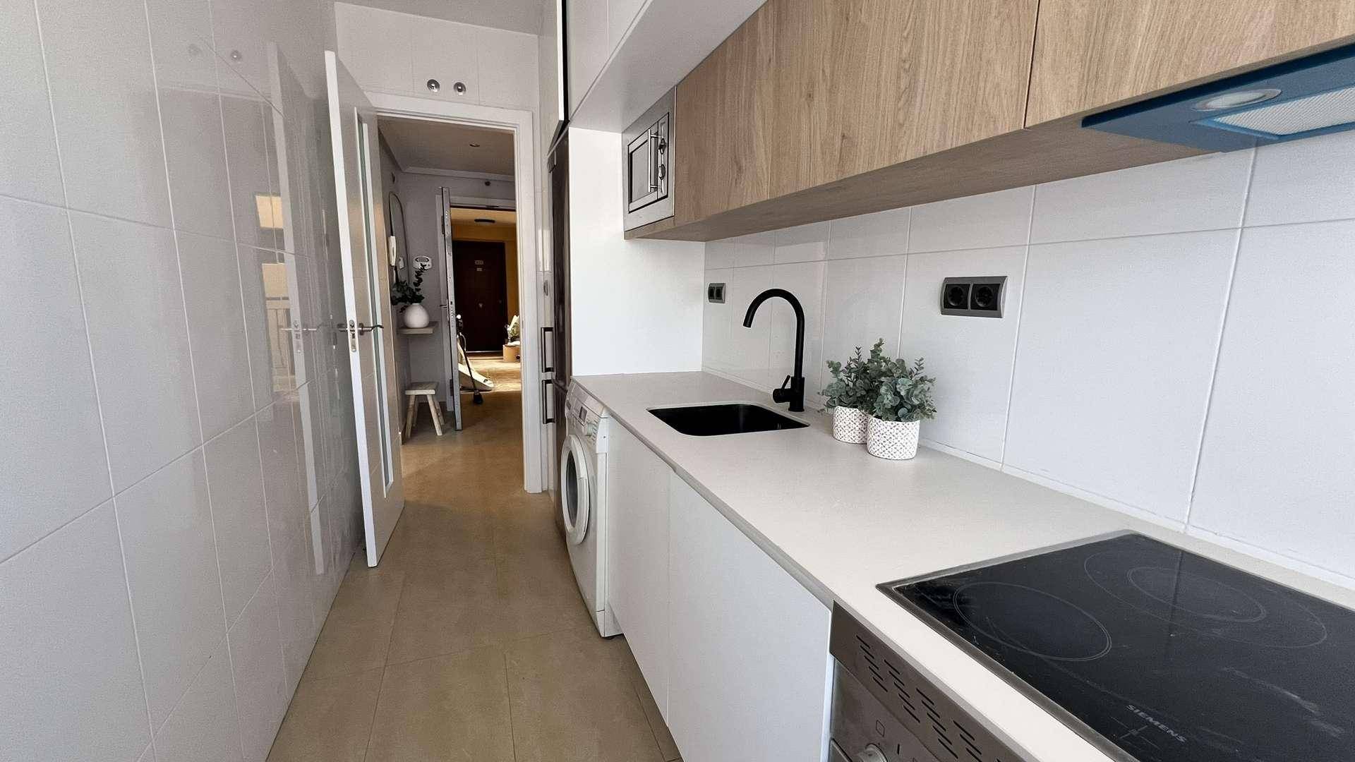 Schmale Küche mit weißen Unterschränken, Holz-Oberschränken und integrierten Geräten.
