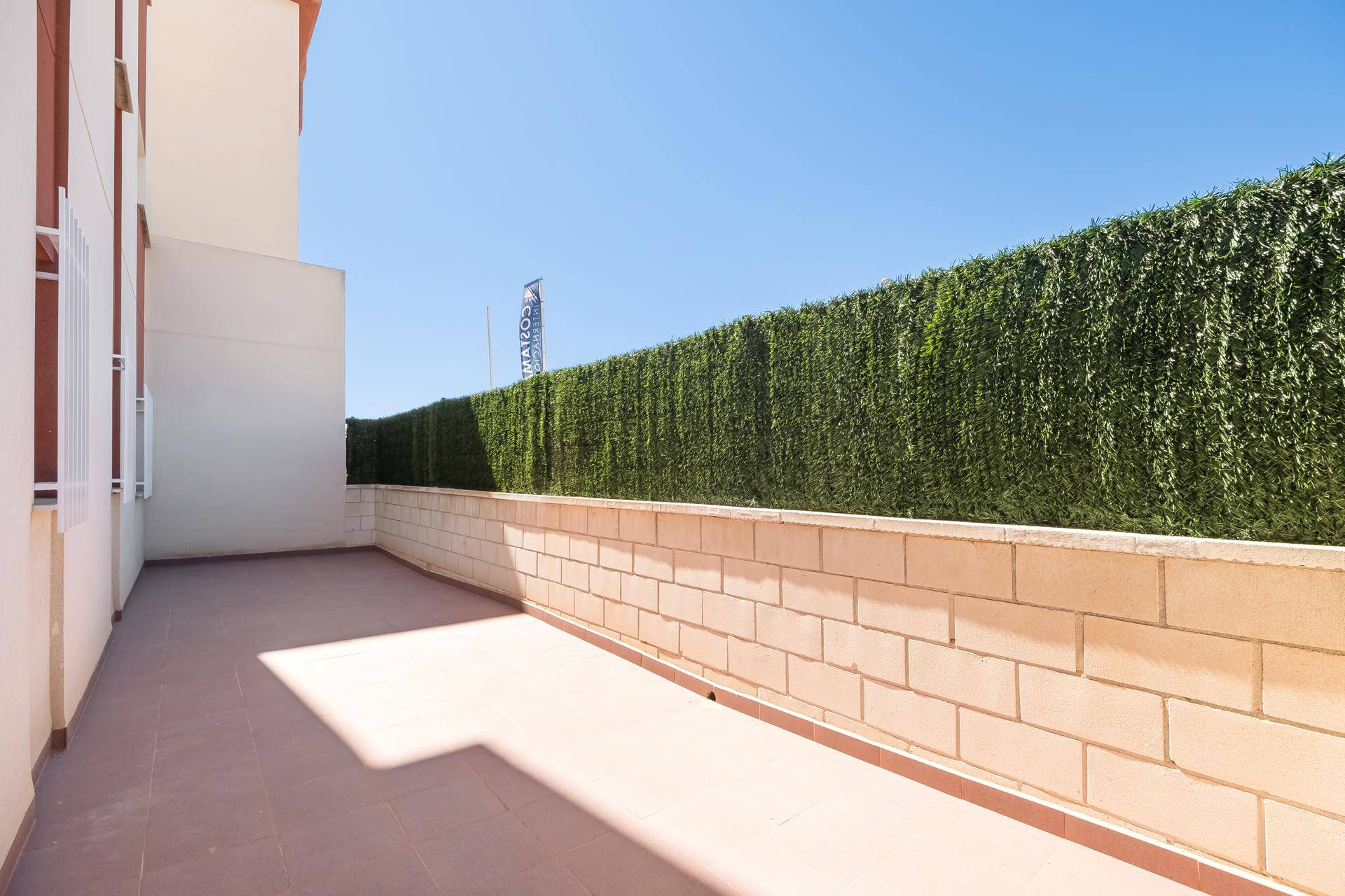 Geräumige Außenterrasse mit hoher Hecke und niedriger Mauer, ideal für Entspannung.
