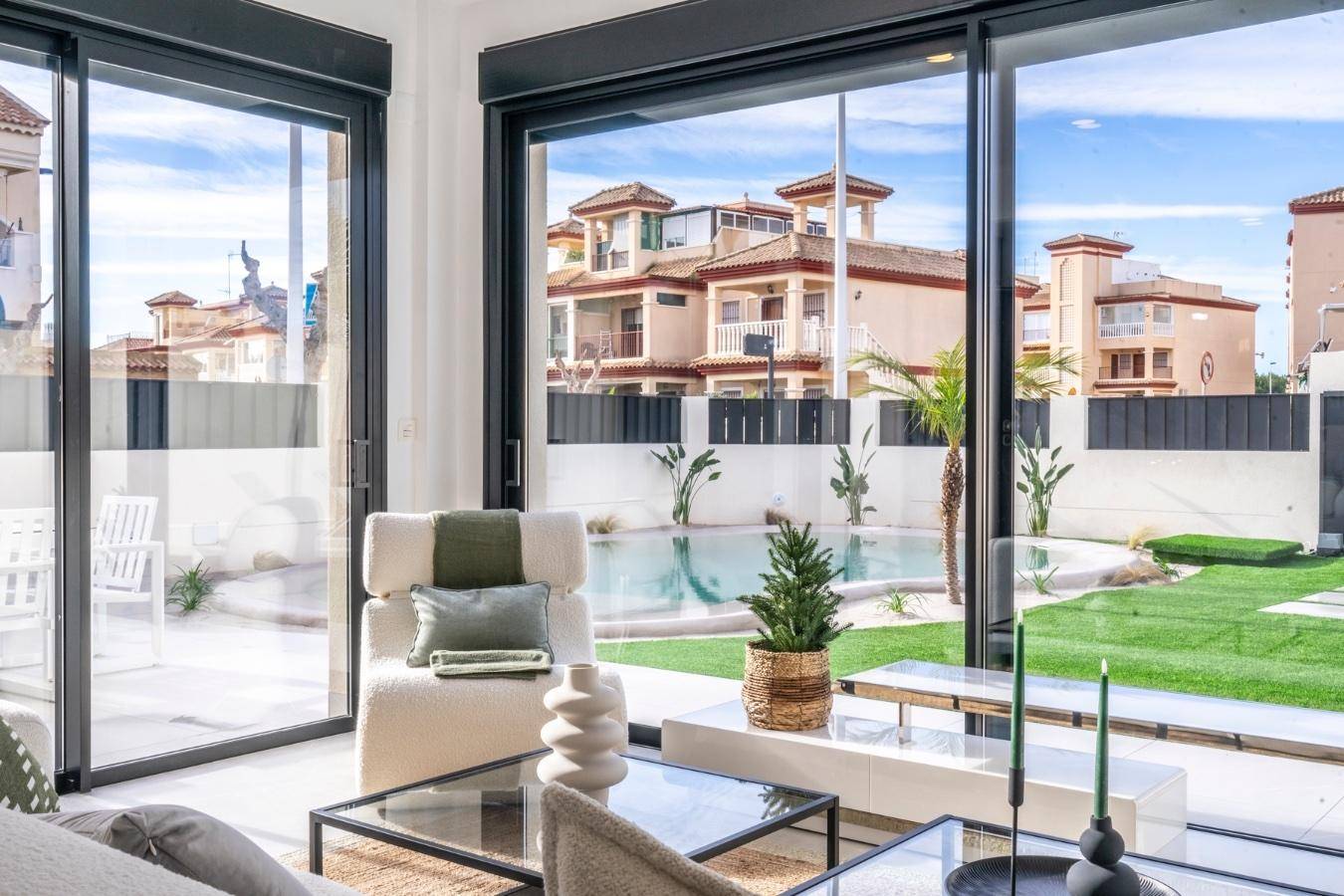 Helles Wohnzimmer mit großen Glasschiebetüren und Blick auf den Garten mit Pool und Nachbarhäusern.
