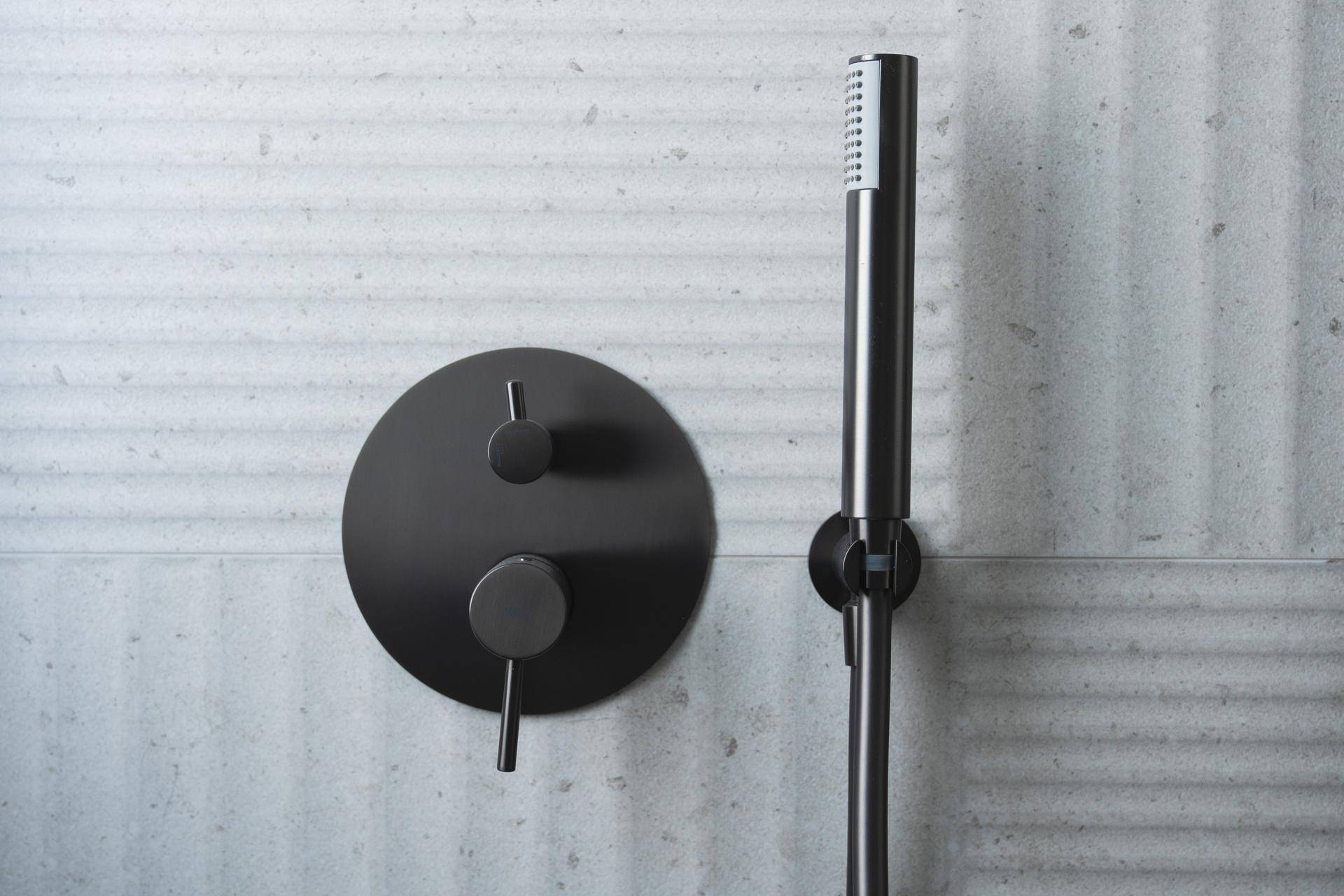 Elegante schwarze Duscharmaturen und Handbrause vor einer strukturierten grauen Wand.