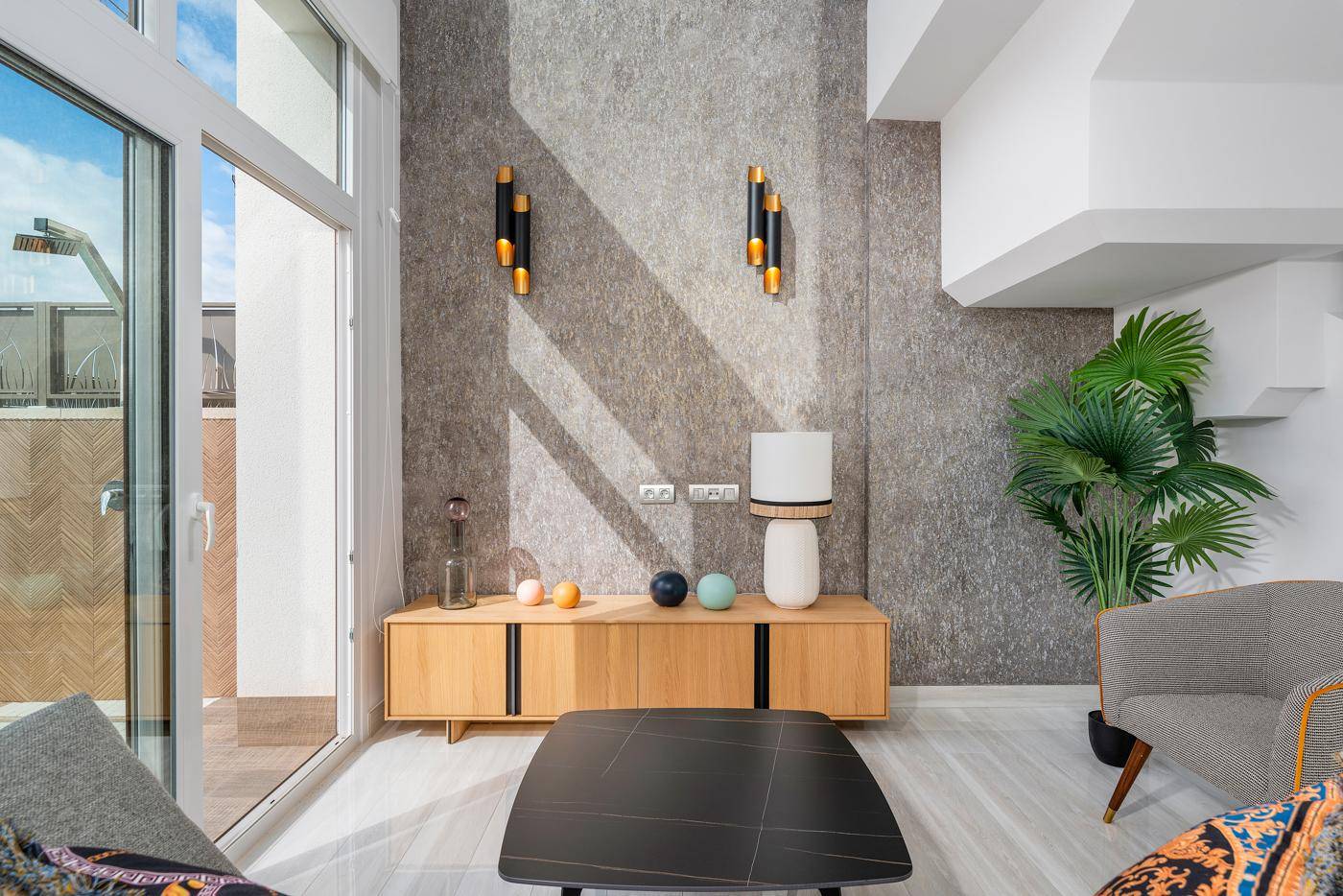 Detailansicht des Wohnzimmers mit strukturierter Wand, modernem Sideboard und Blick auf den Außenbereich.