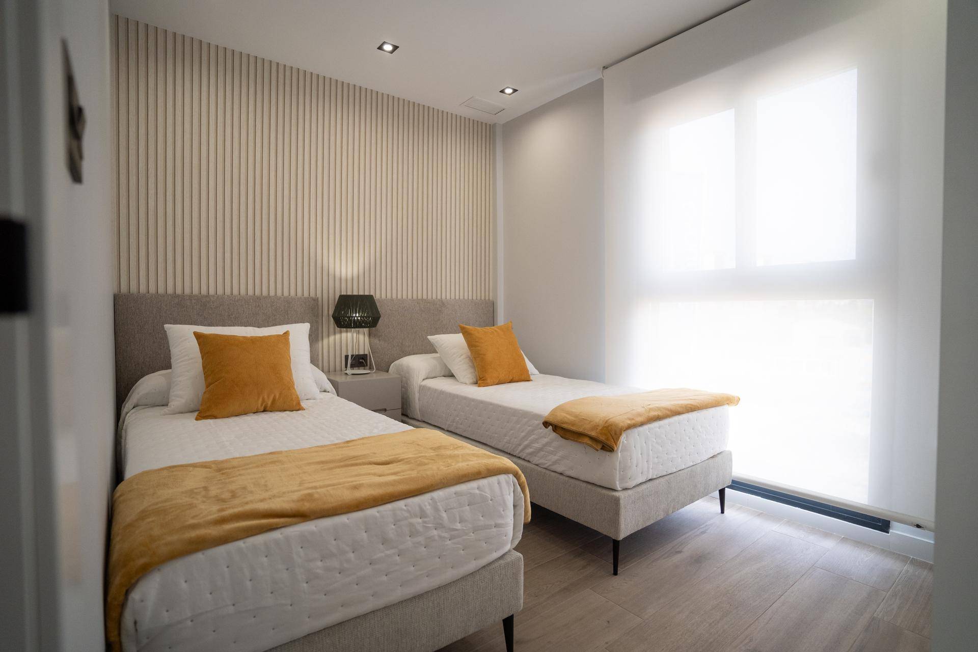 Helles Schlafzimmer mit zwei Einzelbetten, Holzoptikboden und vertikalen Wandpaneelen.