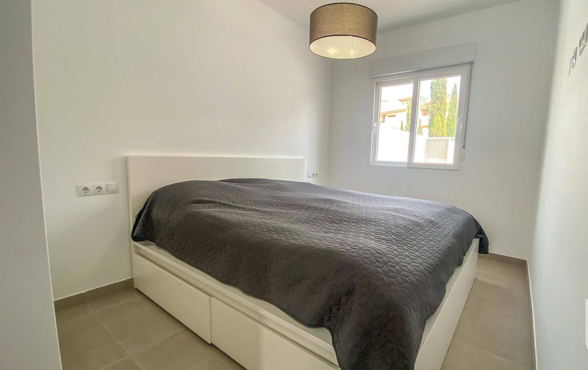 Helles Schlafzimmer mit Doppelbett, Fenster und Fliesenboden.