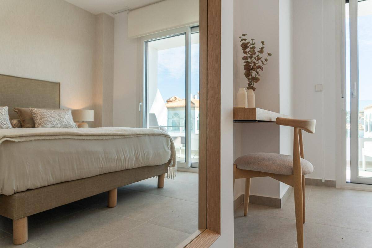 Modernes Schlafzimmer mit Doppelbett, Zugang zum Balkon und kleinem Arbeitsbereich.