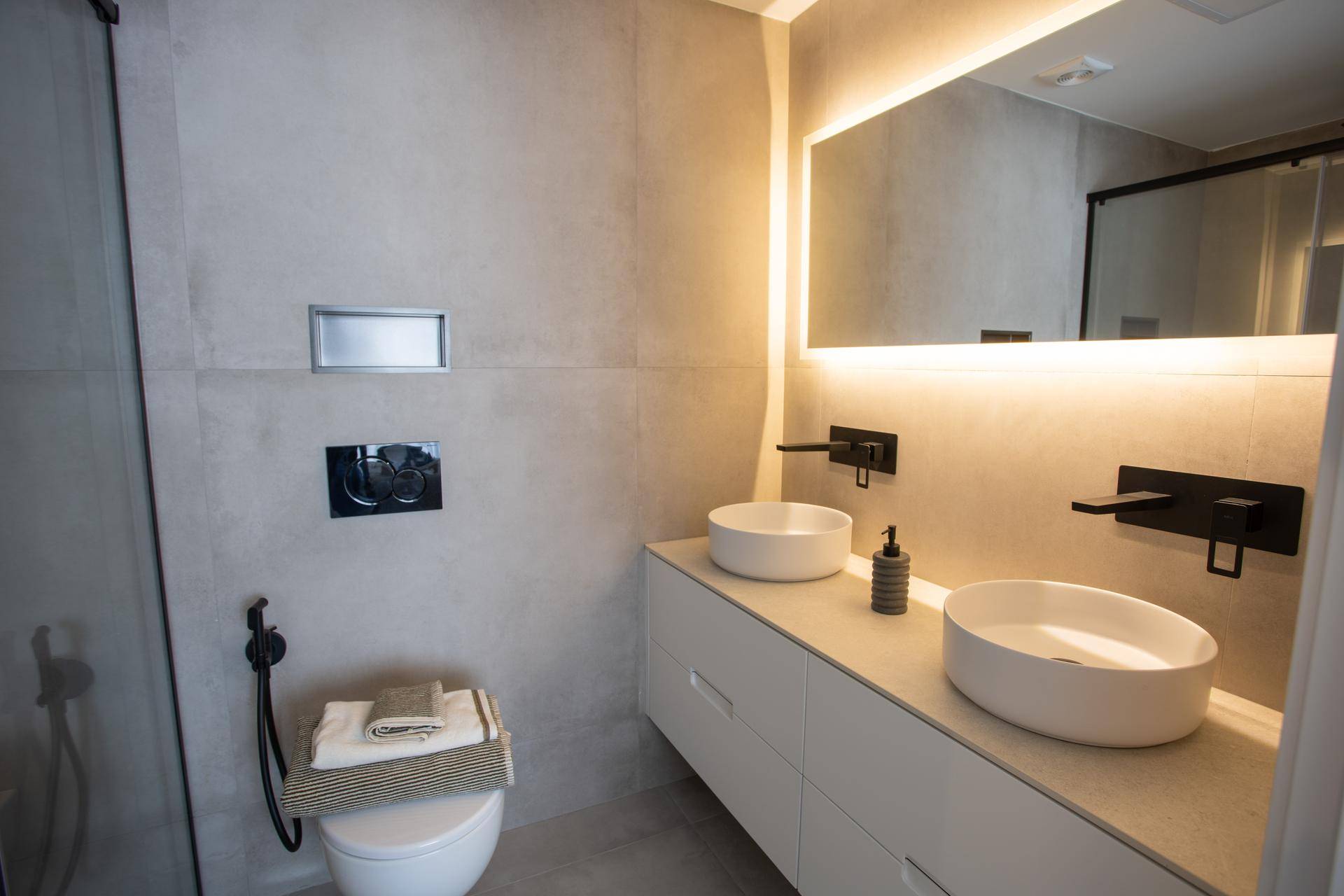 Stilvolles Badezimmer mit Doppelwaschbecken, beleuchtetem Spiegel und Wand-WC.