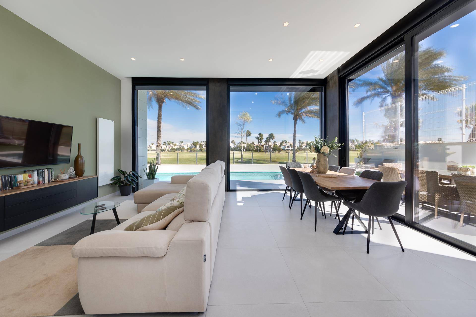 Heller Wohn- und Essbereich mit beigem Sofa und großen Fenstern mit Poolblick.