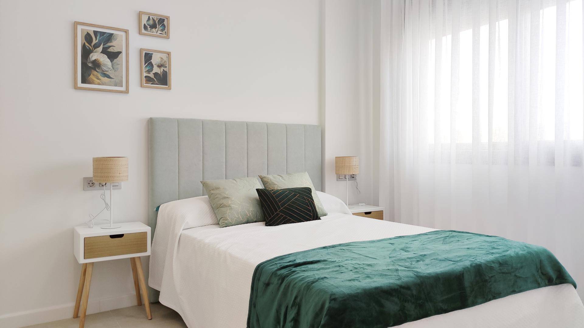 Gemütliches Schlafzimmer mit hellem Bett, grünem Überwurf und großem Fenster mit Vorhängen.