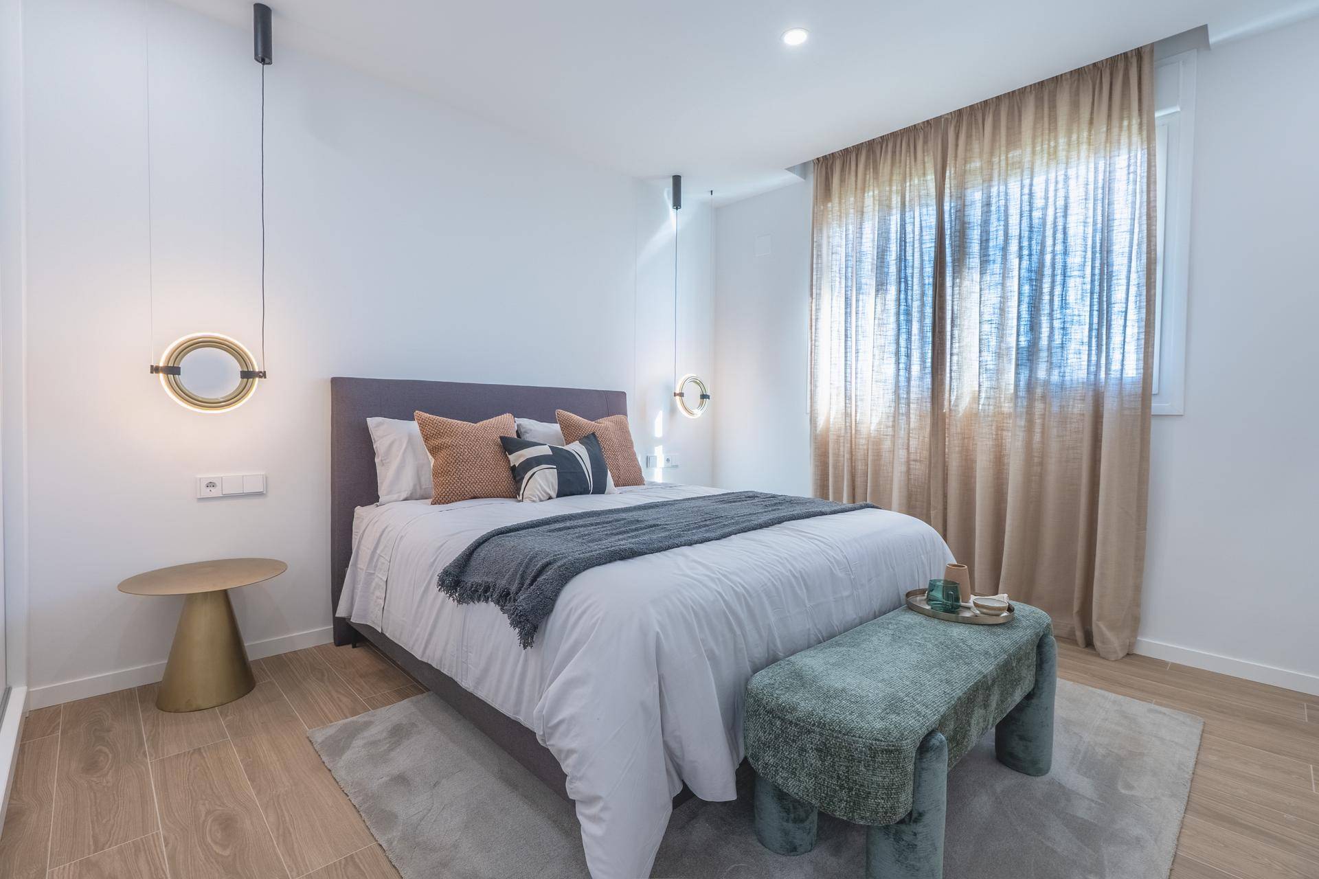 Helles Schlafzimmer mit Doppelbett, Holzboden und Fenster mit Vorhängen.
