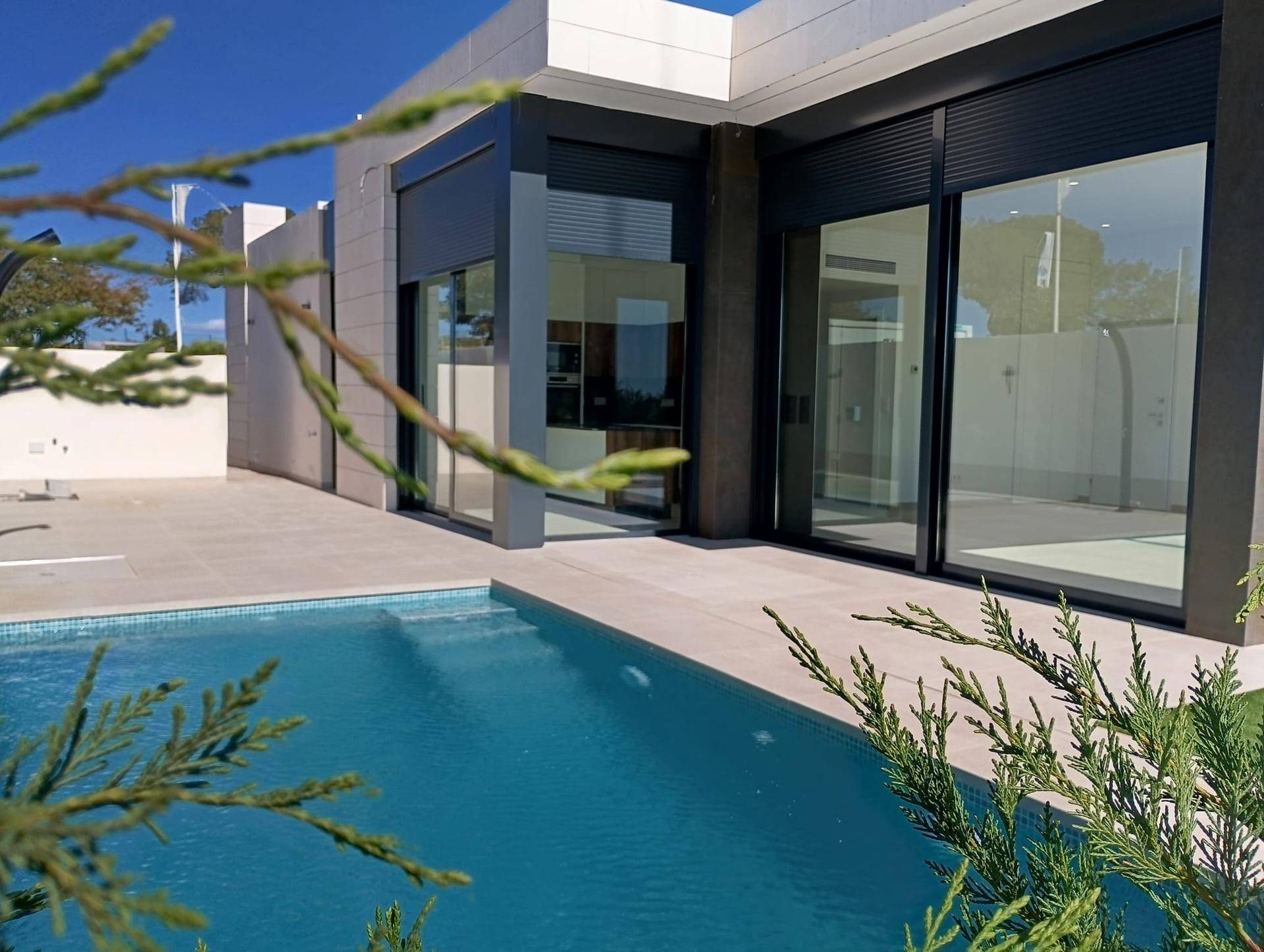 Außenbereich der modernen Villa mit großem Pool, gefliester Terrasse und Blick ins Grüne.