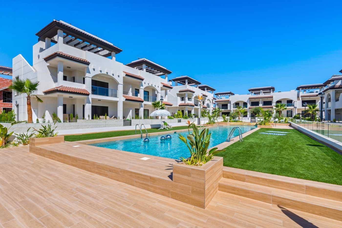 Großzügige Poollandschaft mit Holzterrassen und mediterranen Pflanzen in einer sonnigen Wohnanlage.
