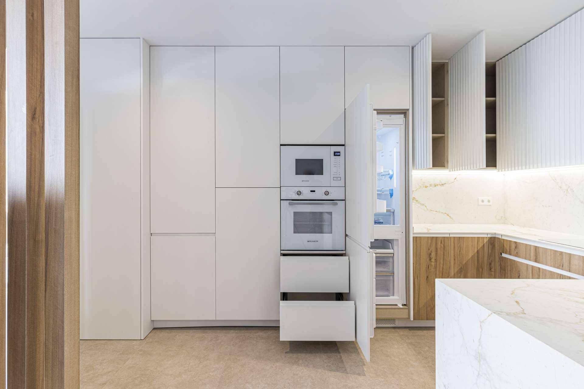 Moderne Einbauküche mit weißen Schränken, integrierten Geräten und eleganten Marmorarbeitsplatten.