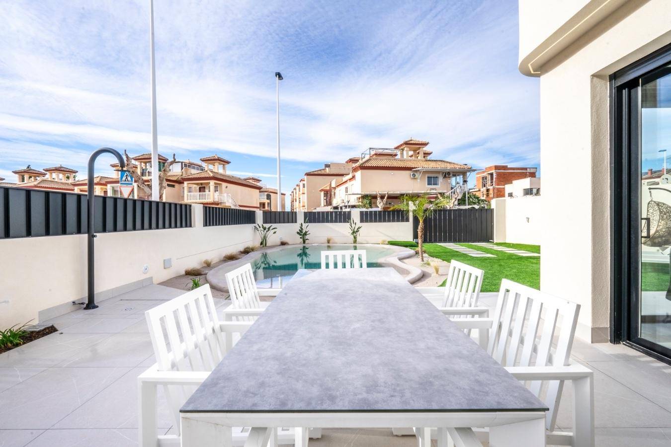 Terrasse mit Esstisch und Stühlen, Blick auf den Pool und den Gartenbereich der modernen Villa.
