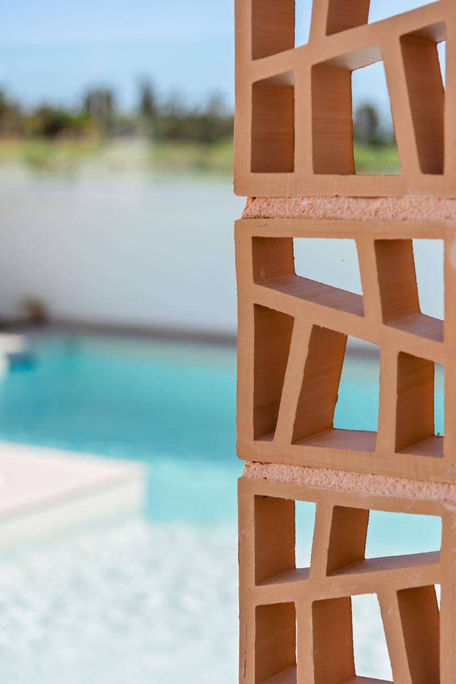 Nahaufnahme einer dekorativen Trennwand aus Holz mit dem Pool im Hintergrund.