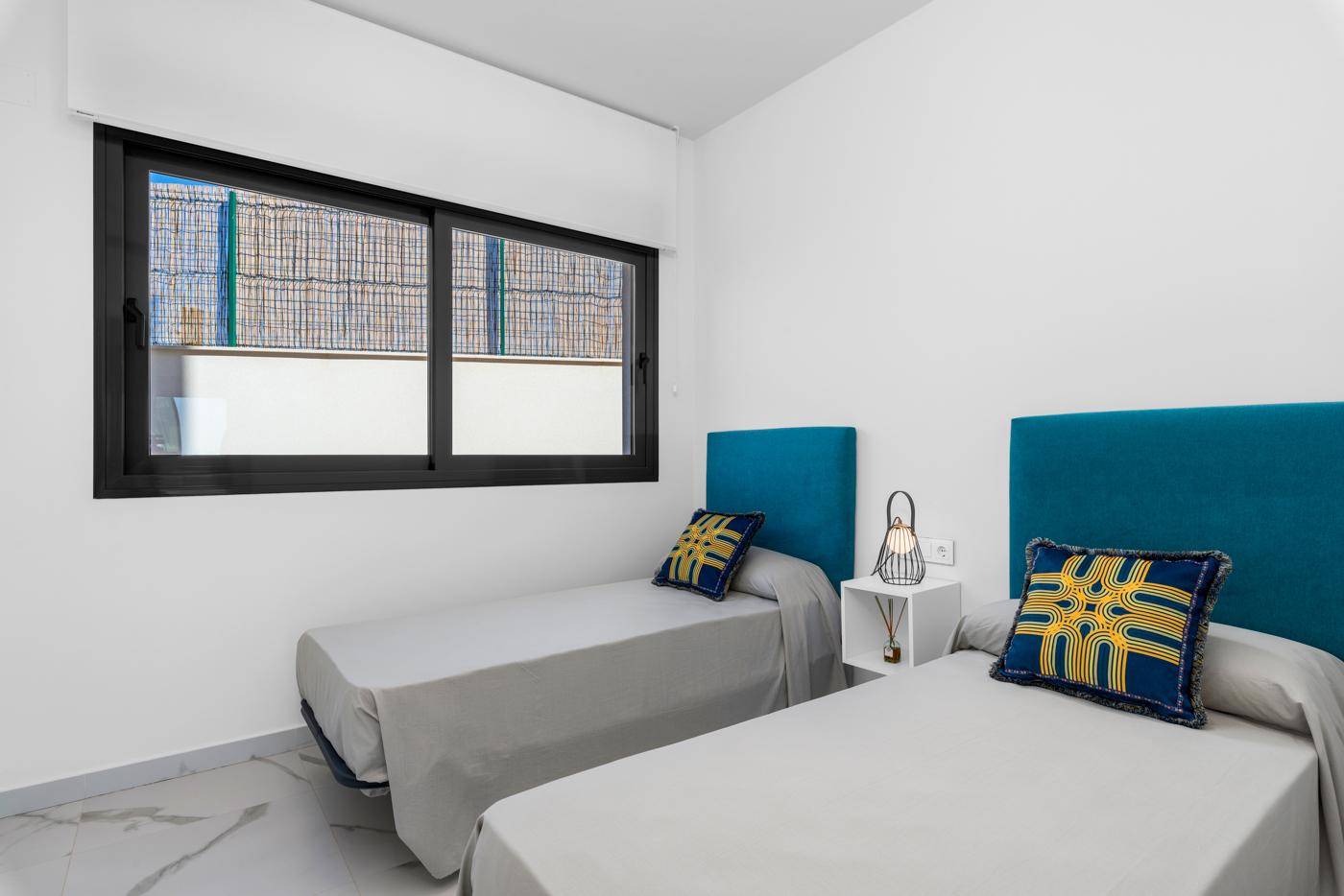 Modernes Schlafzimmer mit zwei Einzelbetten, farbigen Kopfteilen und Fenster.