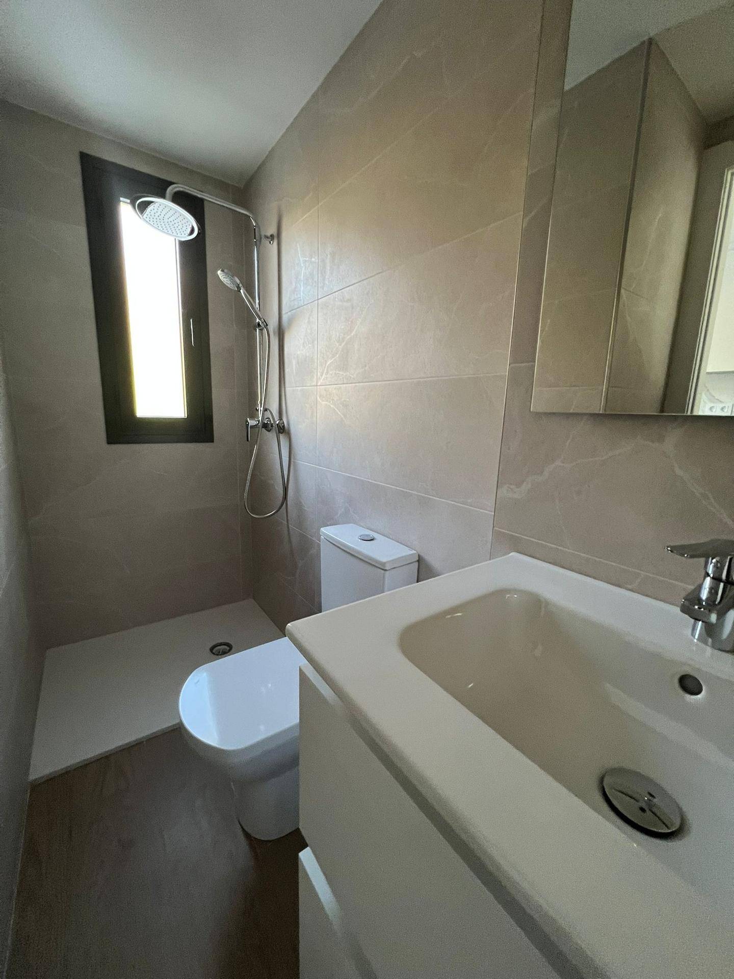 Modernes Badezimmer mit ebenerdiger Dusche, WC und Waschtisch mit Spiegel.