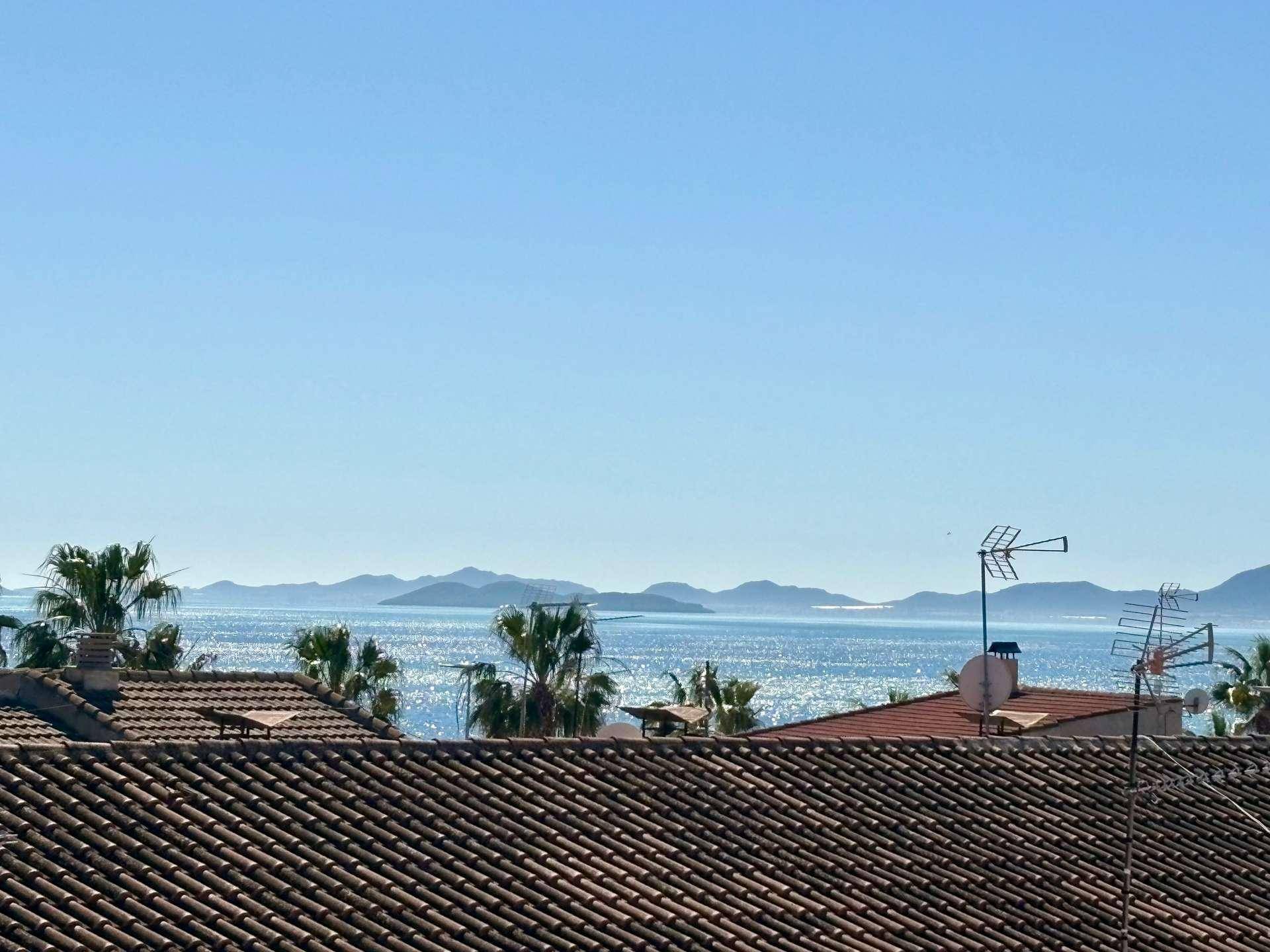 Weitblick über Dächer und das glitzernde Meer mit fernen Inseln am Horizont.