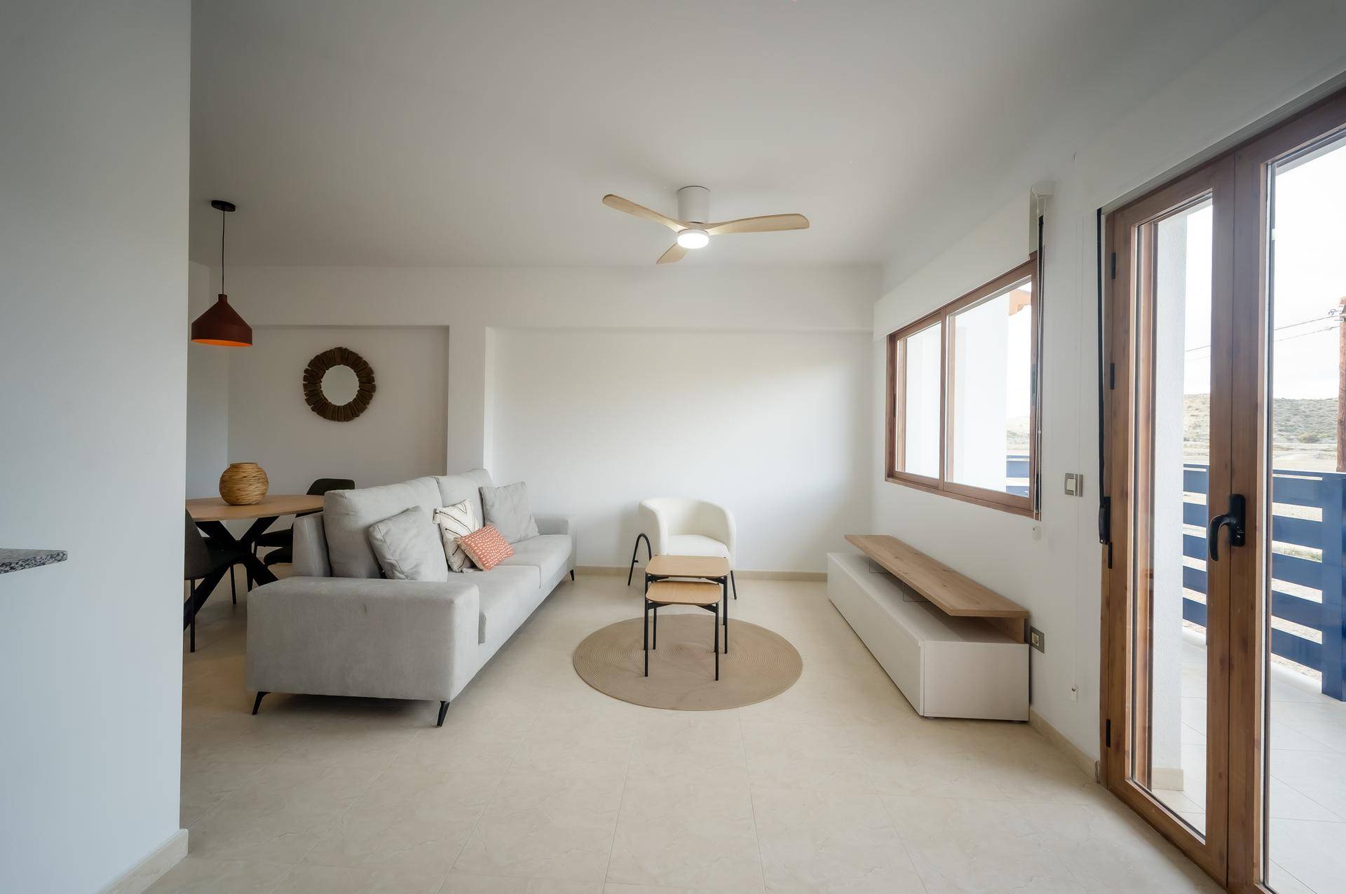Heller Wohn- und Essbereich mit beigem Fliesenboden, Deckenventilator und Zugang zum Balkon.