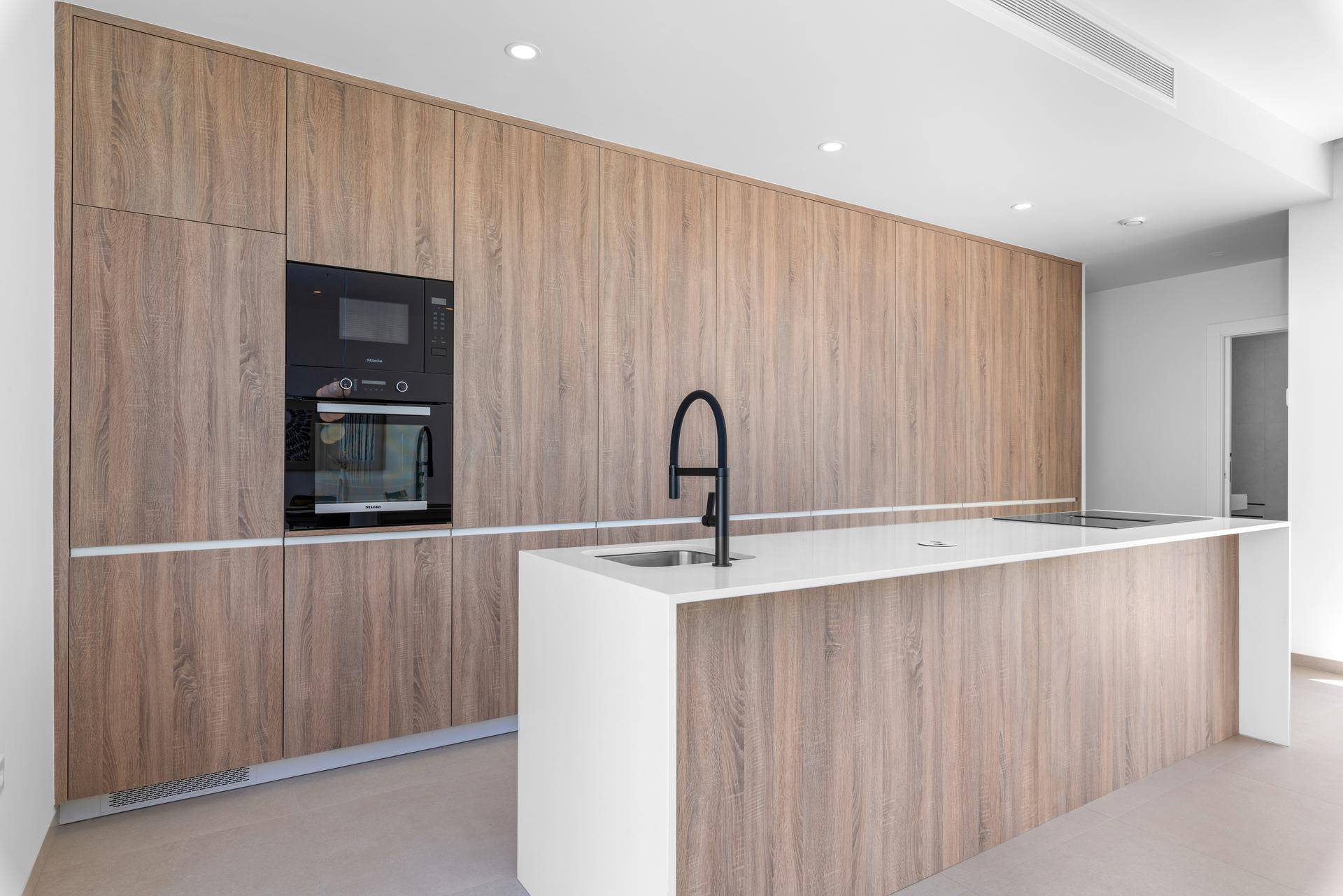 Moderne Einbauküche mit holzfarbenen Schränken, weißer Arbeitsplatte und integrierten Geräten.