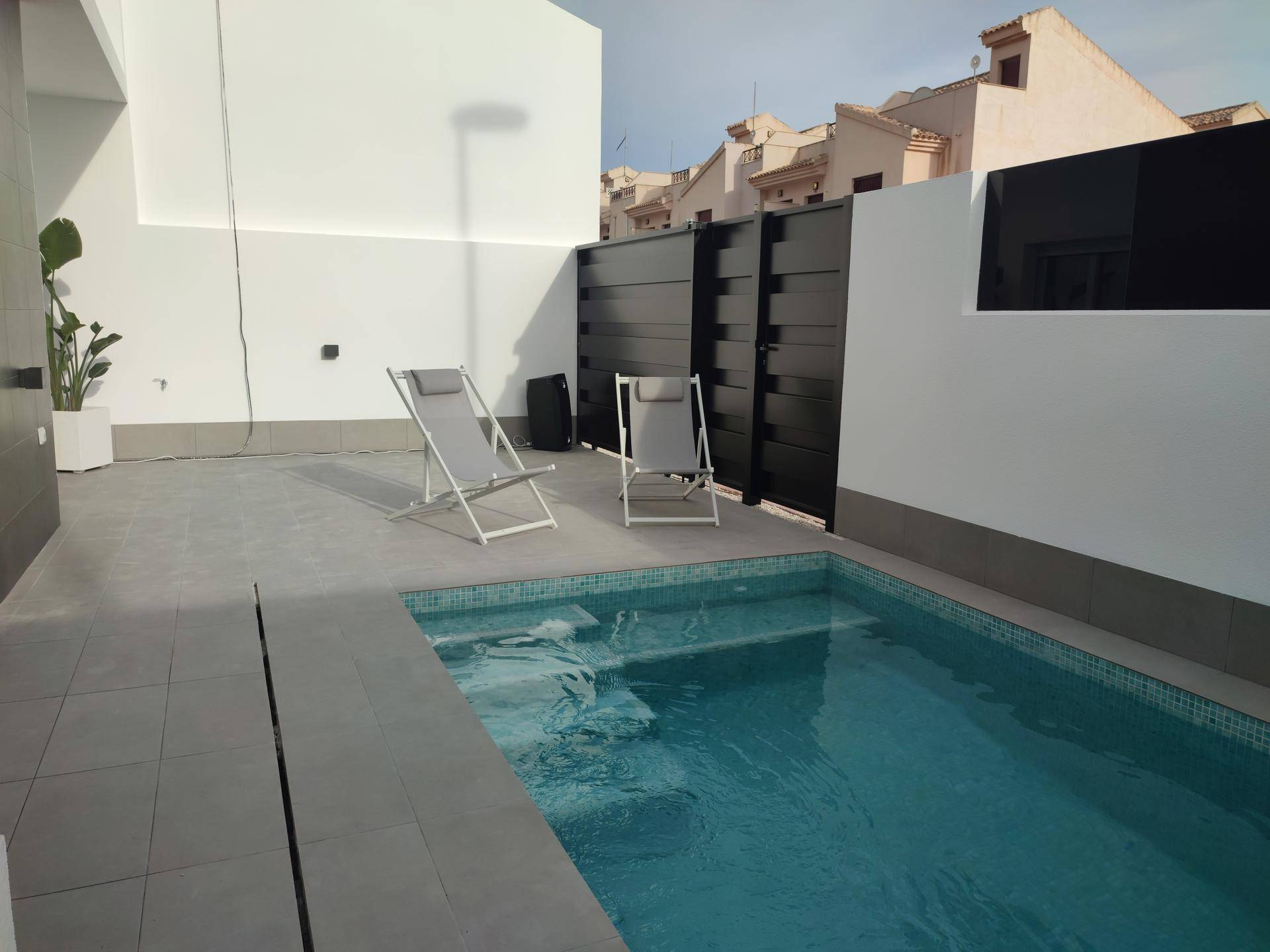 Kleiner privater Poolbereich mit Liegestühlen und einer modernen schwarzen Zaunanlage im Hintergrund.