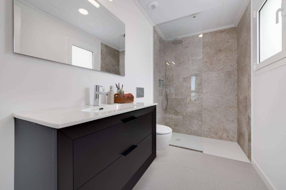 Modernes Badezimmer mit begehbarer Dusche, dunklem Waschtisch und Fenster für Tageslicht.