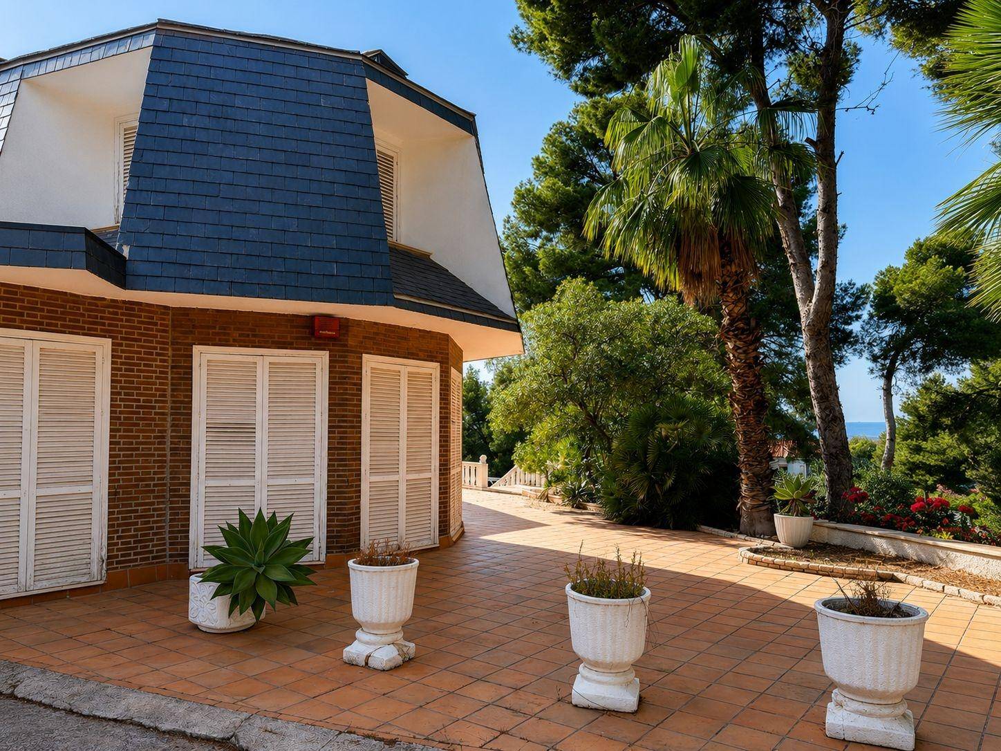 Detailansicht der Villa mit Mansarddach und einer weitläufigen Terrasse, umgeben von mediterraner Vegetation.