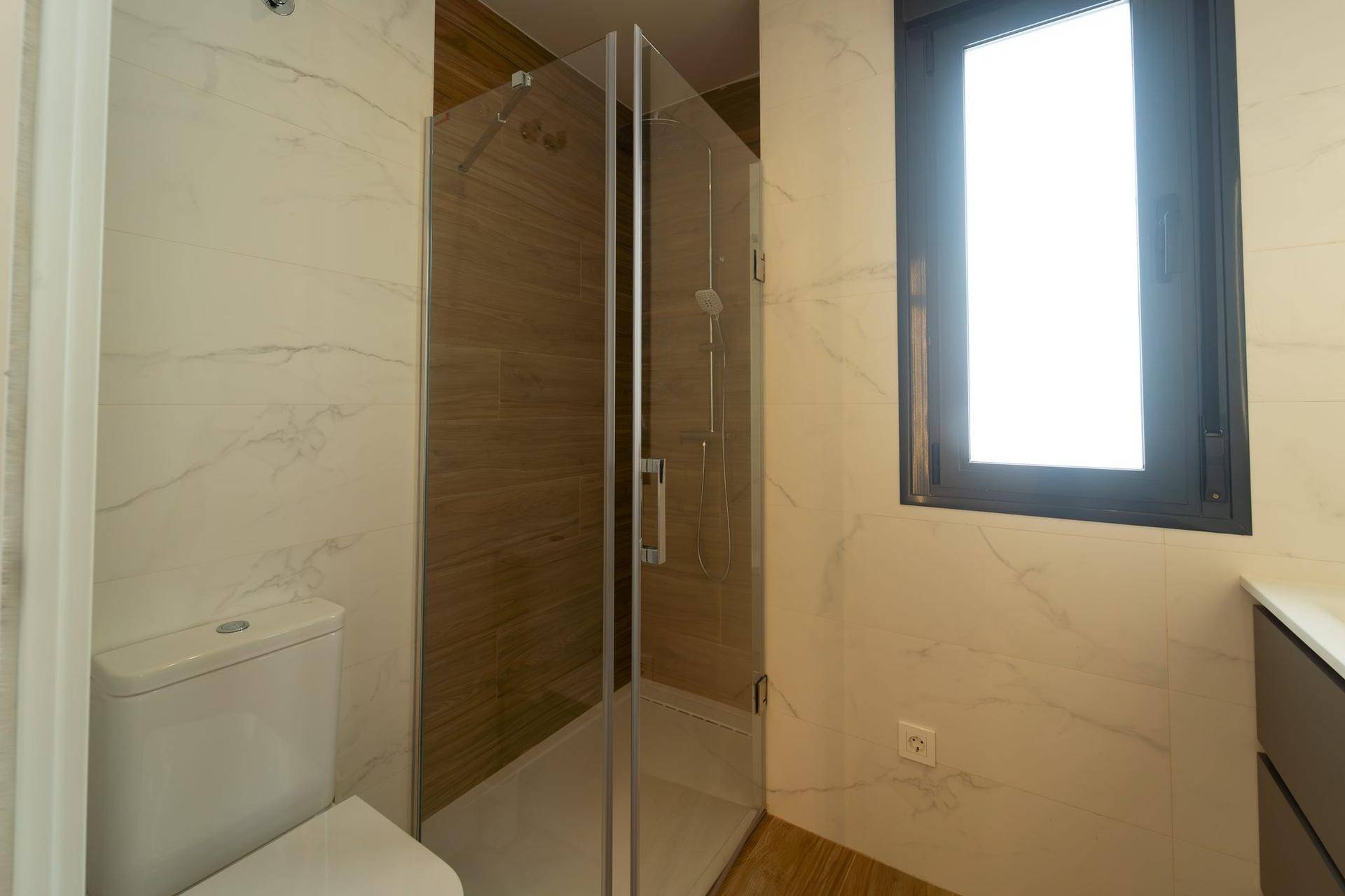 Helles Badezimmer mit Duschkabine, Toilette und Fenster für natürliche Belüftung.