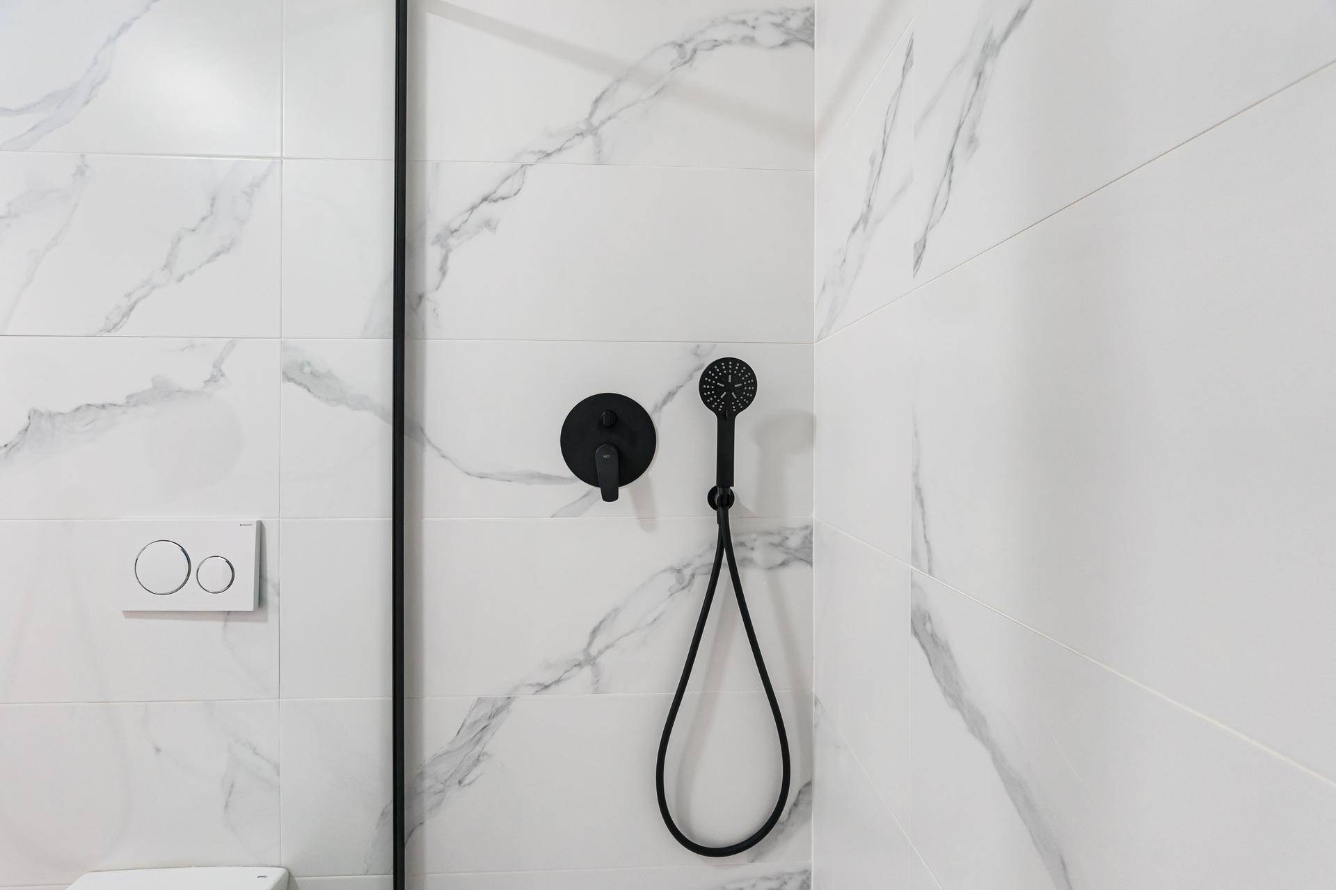 Duschbereich im modernen Badezimmer mit schwarzen Armaturen und weißen Marmor-Effektfliesen.