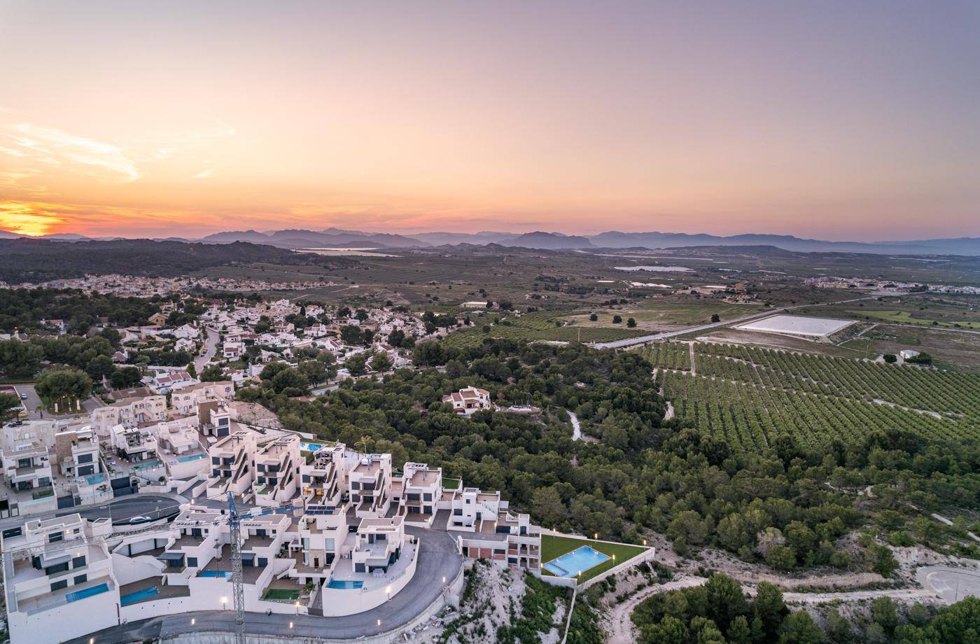 Wohnanlage mit modernen Häusern und Pools, umgeben von weiten Landschaften bei Sonnenuntergang.