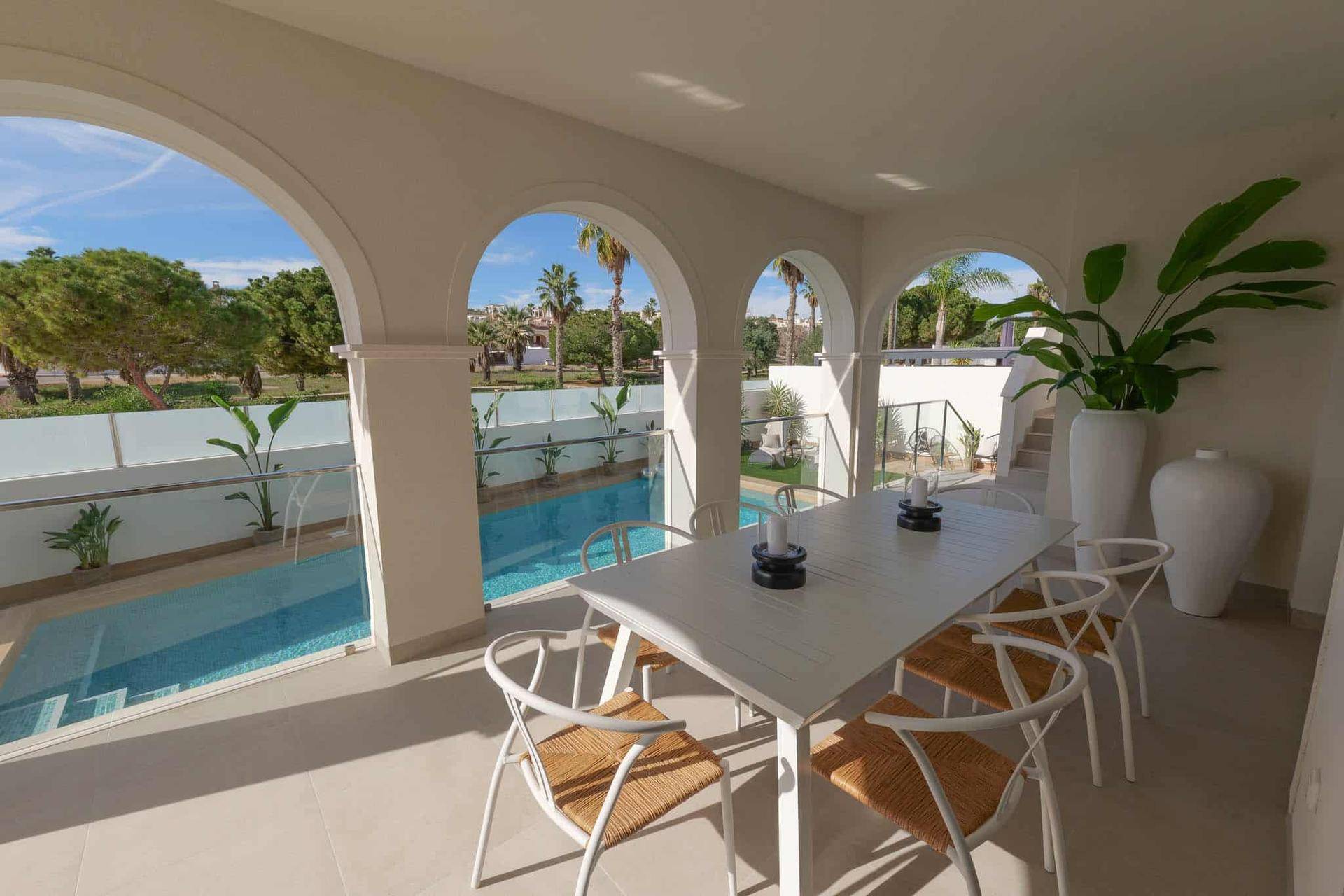 Überdachte Terrasse mit Esstisch und Stühlen, bietet einen schönen Blick auf den Pool und die Palmen.
