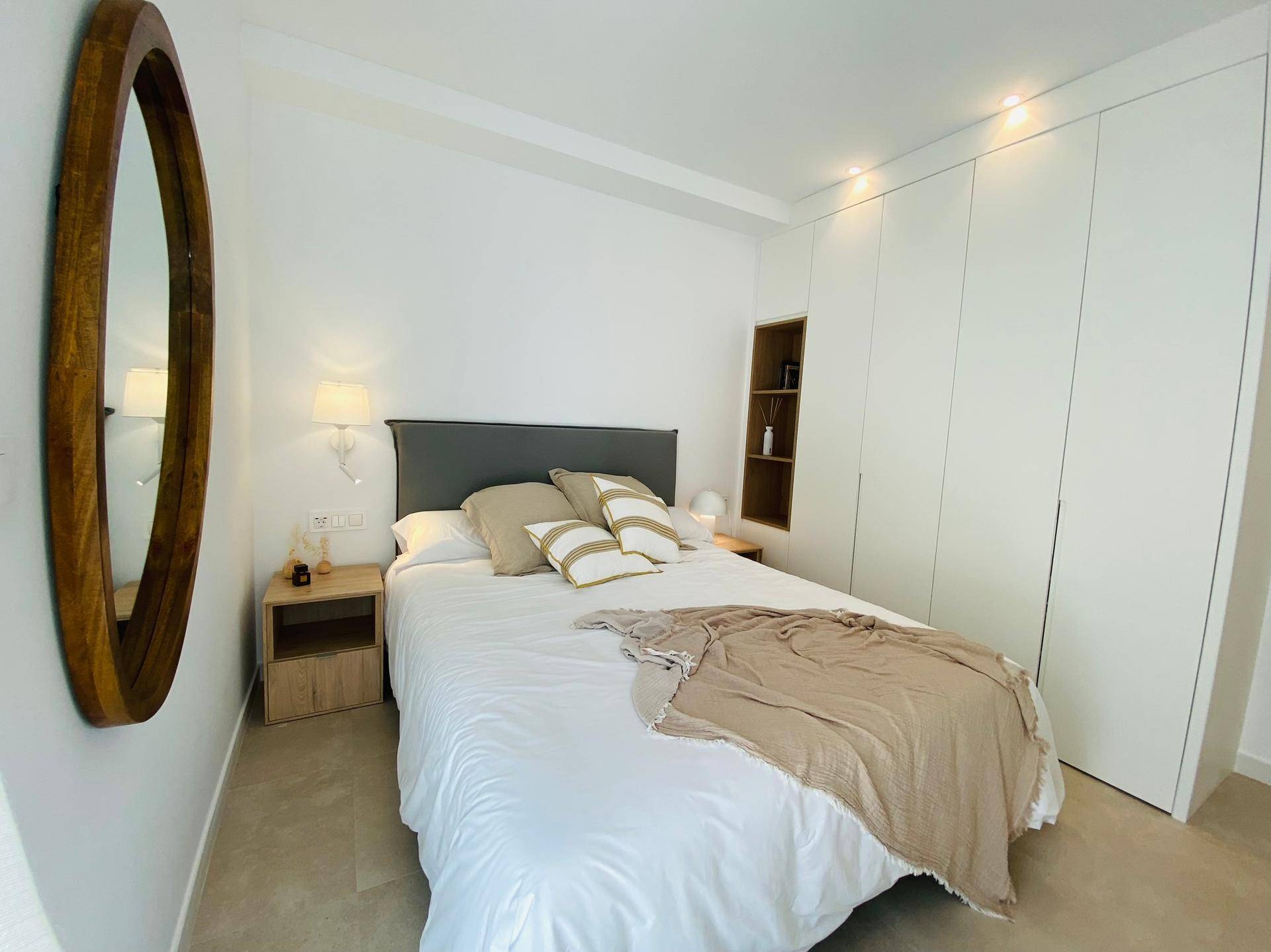 Helles Schlafzimmer mit Doppelbett, Einbauschränken und modernem Spiegel.