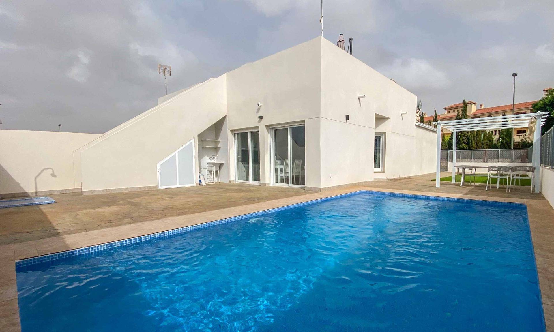 Modernes Haus mit großem Poolbereich und gepflasterter Terrasse unter bewölktem Himmel.