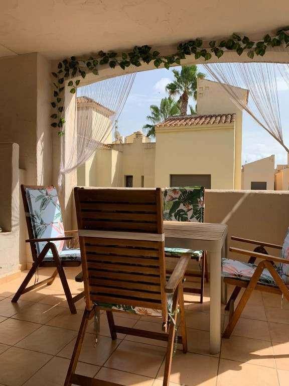 Sonniger Balkon mit Esstisch und Stühlen, umgeben von mediterraner Architektur und Palmen.