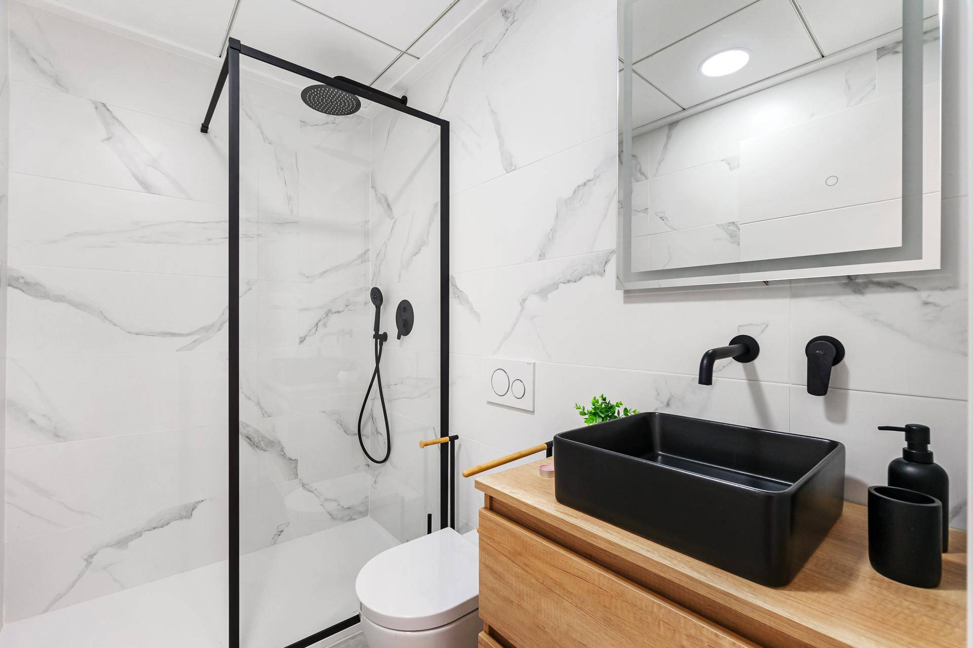 Modernes Badezimmer mit begehbarer Dusche, schwarzem Waschbecken und weißen Marmorfliesen.
