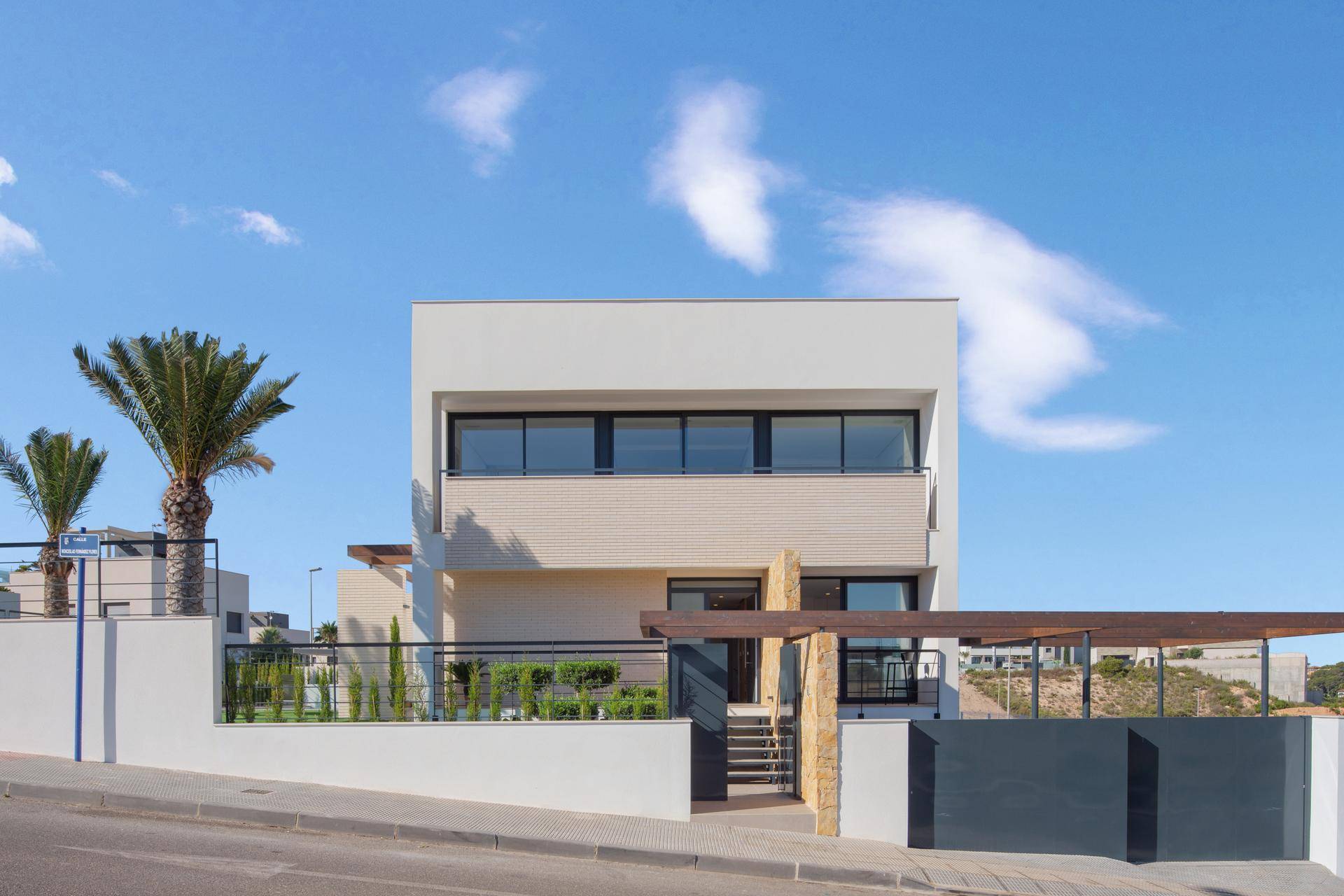 Moderne weiße Fassade der Villa von der Straße aus gesehen mit gepflegtem Vorgarten und Palmen.