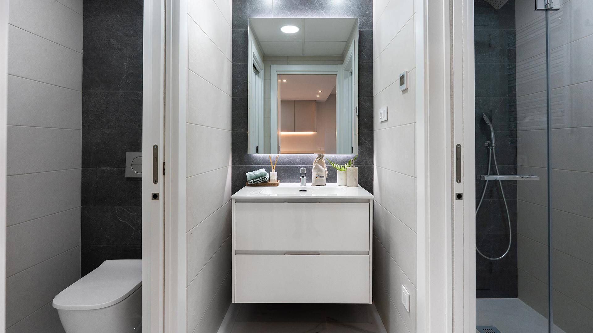 Modernes Badezimmer mit schwebendem Waschtisch, beleuchtetem Spiegel und ebenerdiger Dusche.
