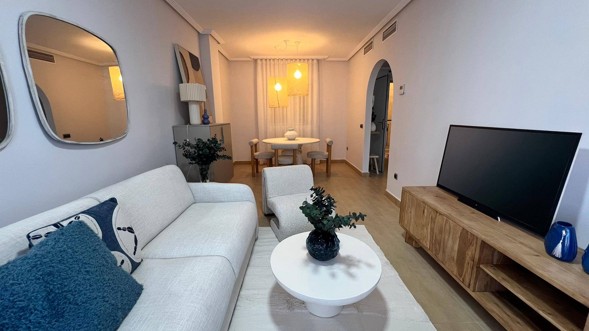 Gemütlicher Wohnbereich mit Sofa, Fernseher und Essbereich im Hintergrund, modern eingerichtet.