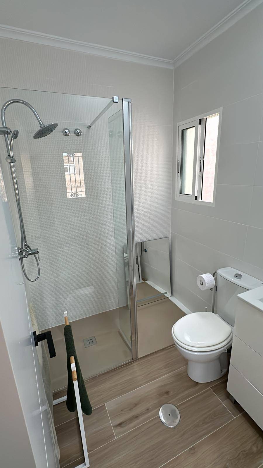 Modernes Badezimmer mit begehbarer Dusche, WC und Fenster für Tageslicht.