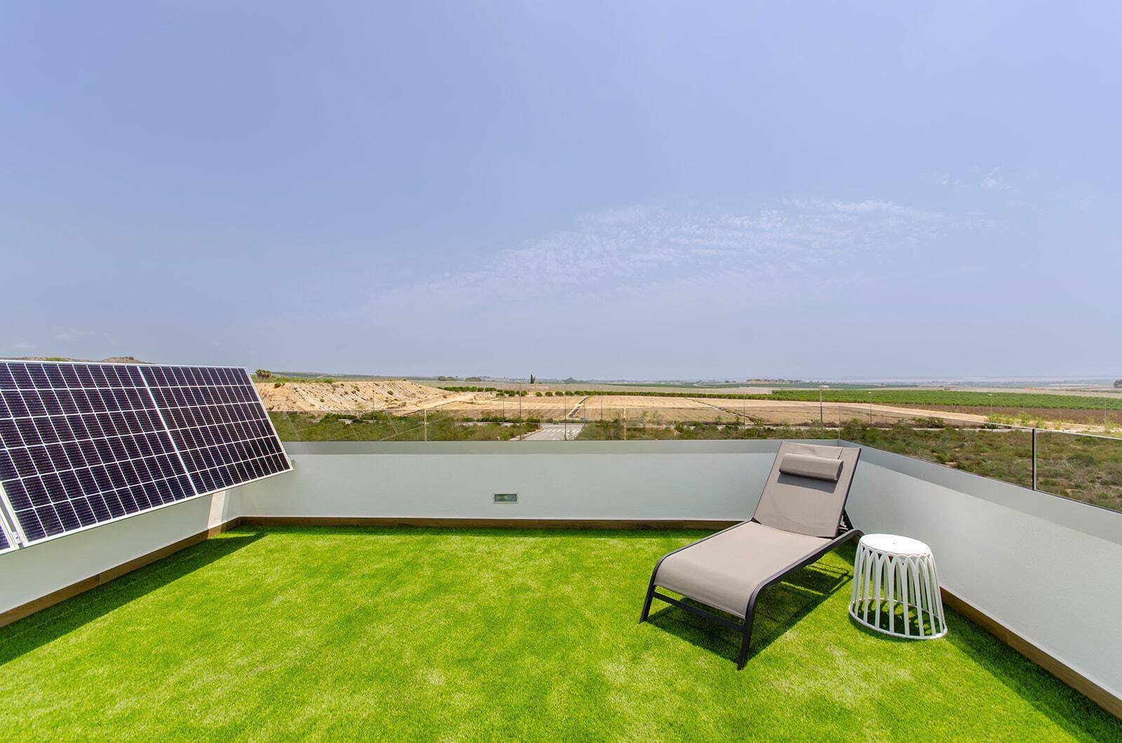 Sonniger Dachterrasse mit Kunstrasen, Liegestuhl und Photovoltaik-System.