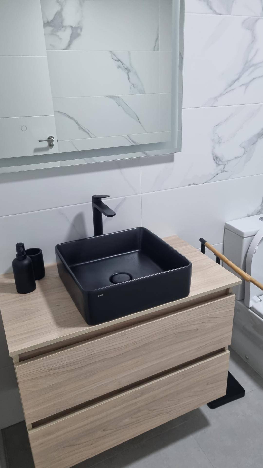 Badezimmer mit modernem Waschbecken auf Holzunterschrank und Marmorfliesen.