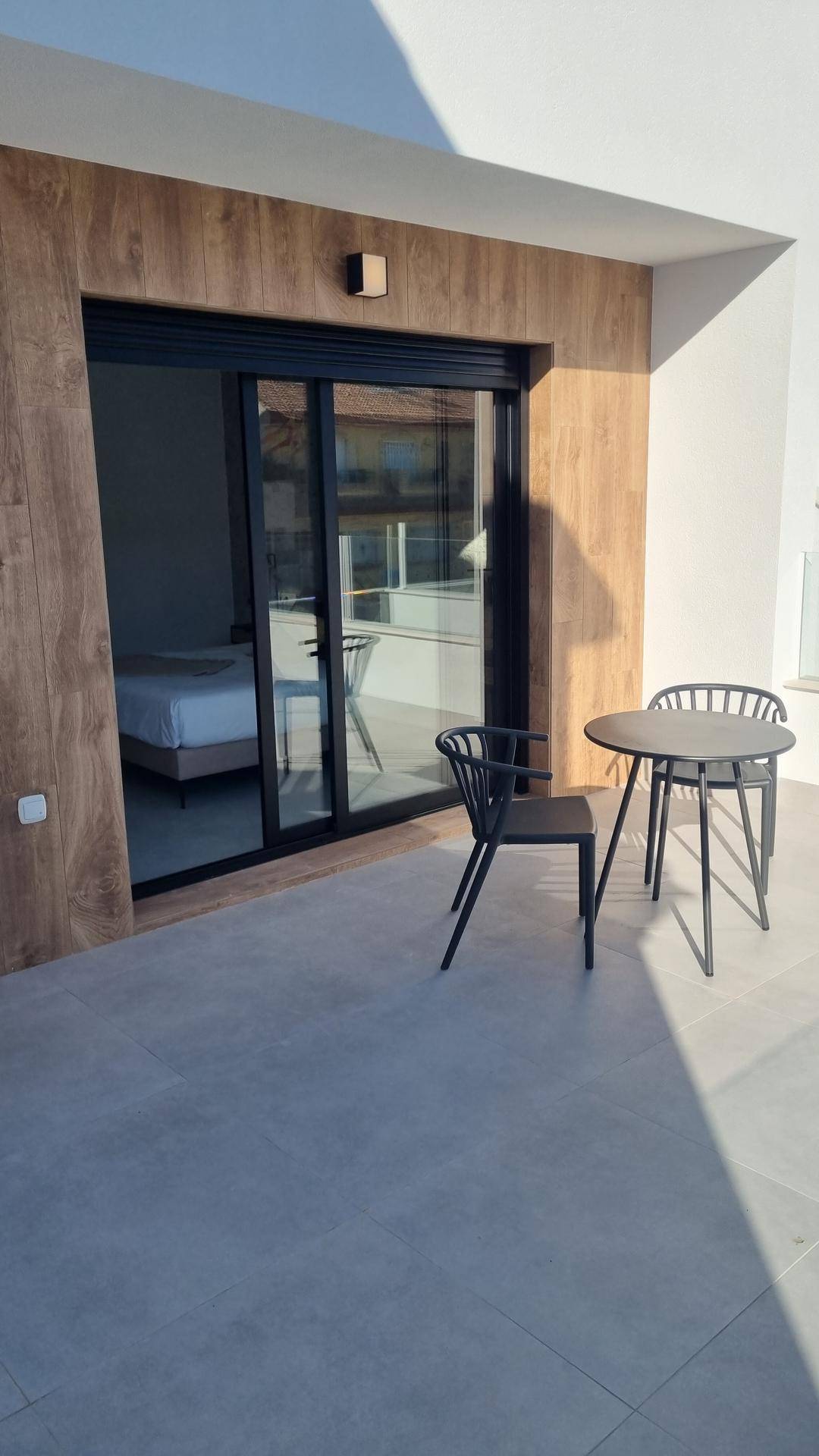 Kleiner Balkon mit Sitzgelegenheiten und Zugang zu einem Schlafzimmer, umgeben von Holzverkleidung.