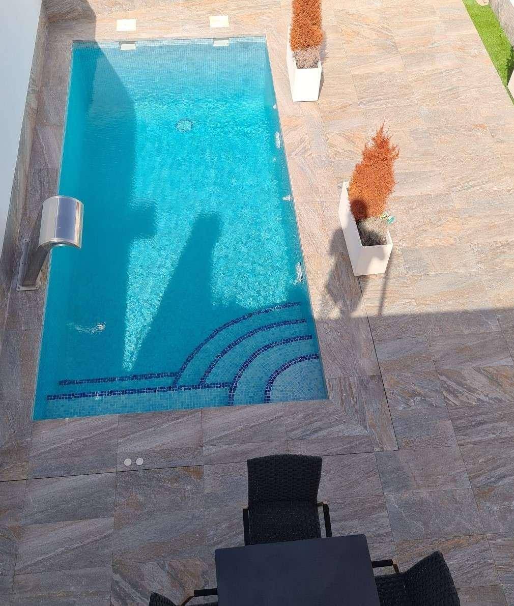 Vogelperspektive auf den rechteckigen Pool und die großzügige, geflieste Terrasse.