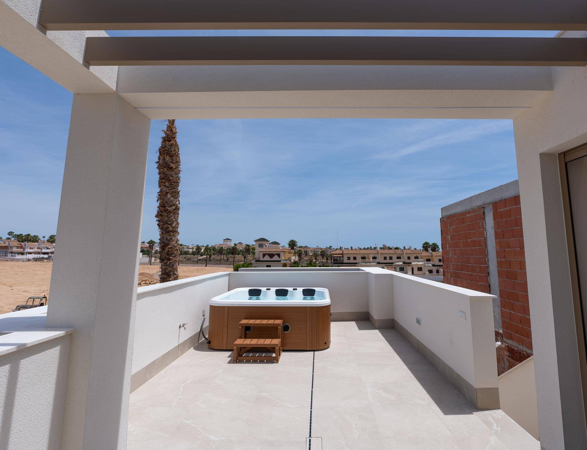 Dachterrasse mit Whirlpool und Pergola, die Schatten spendet, unter blauem Himmel.